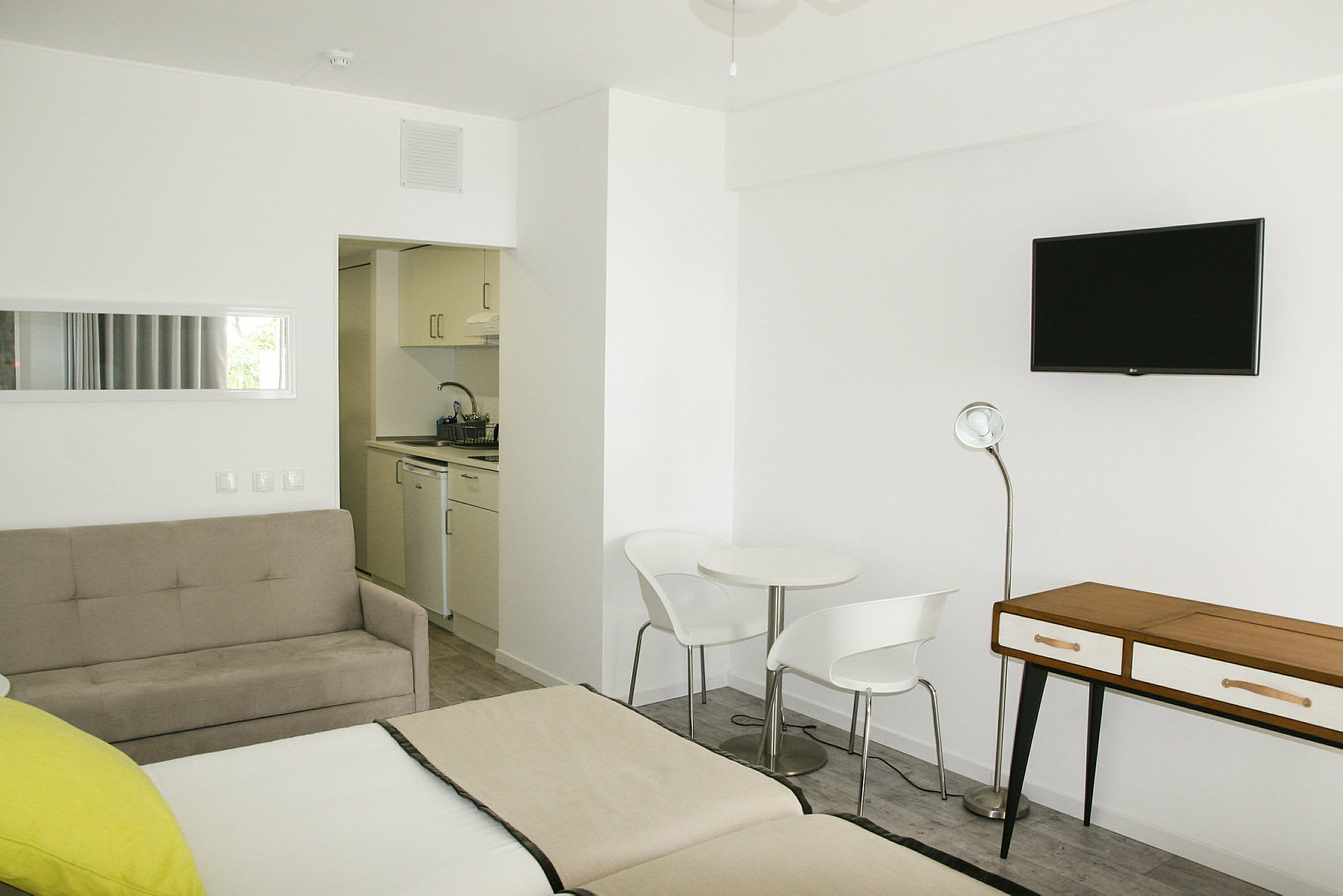 Ett modernt hotellrum med vita väggar, en sittgrupp och ett mindre kök. (AI-genererad text)