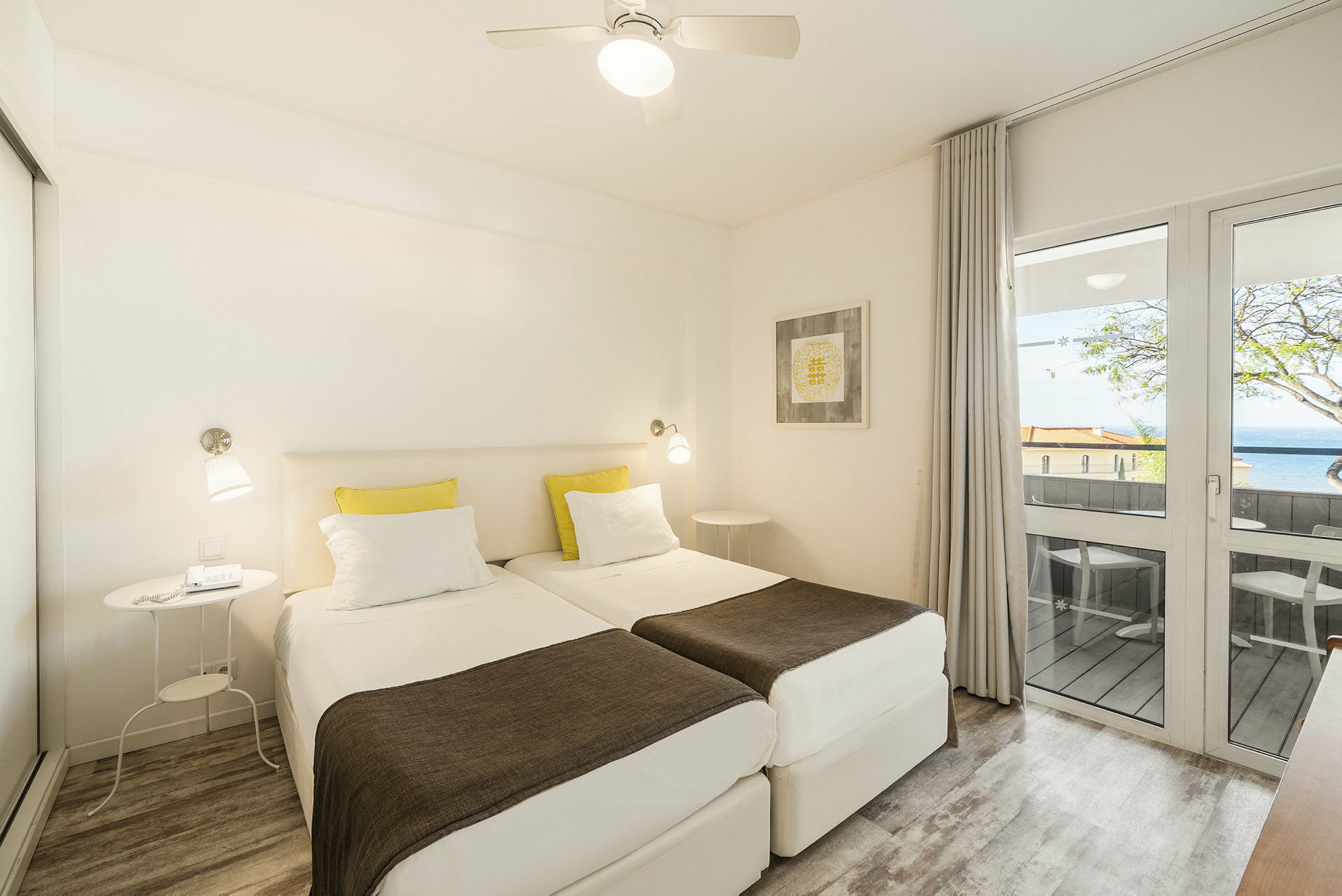 Ett hotellrum med två enkelsängar, en balkong med utsikt och ljusa möbler. (AI-genererad text)