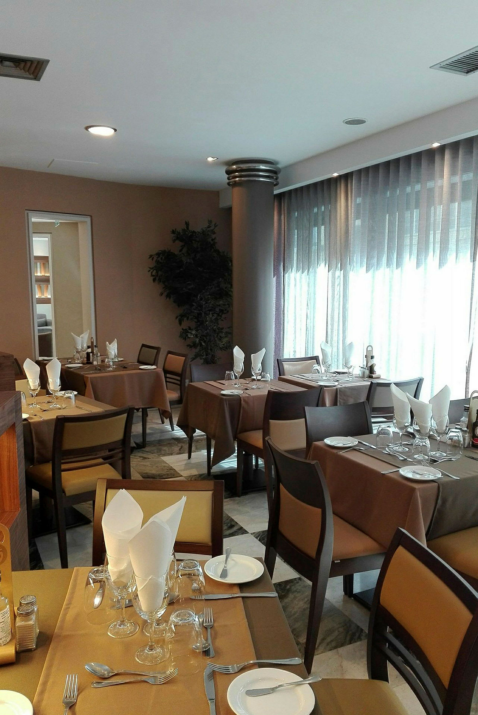 Ett inomhusområde i en restaurang med dukade bord, bruna dukar och stolar med ljusbruna kuddar. (AI-genererad text)