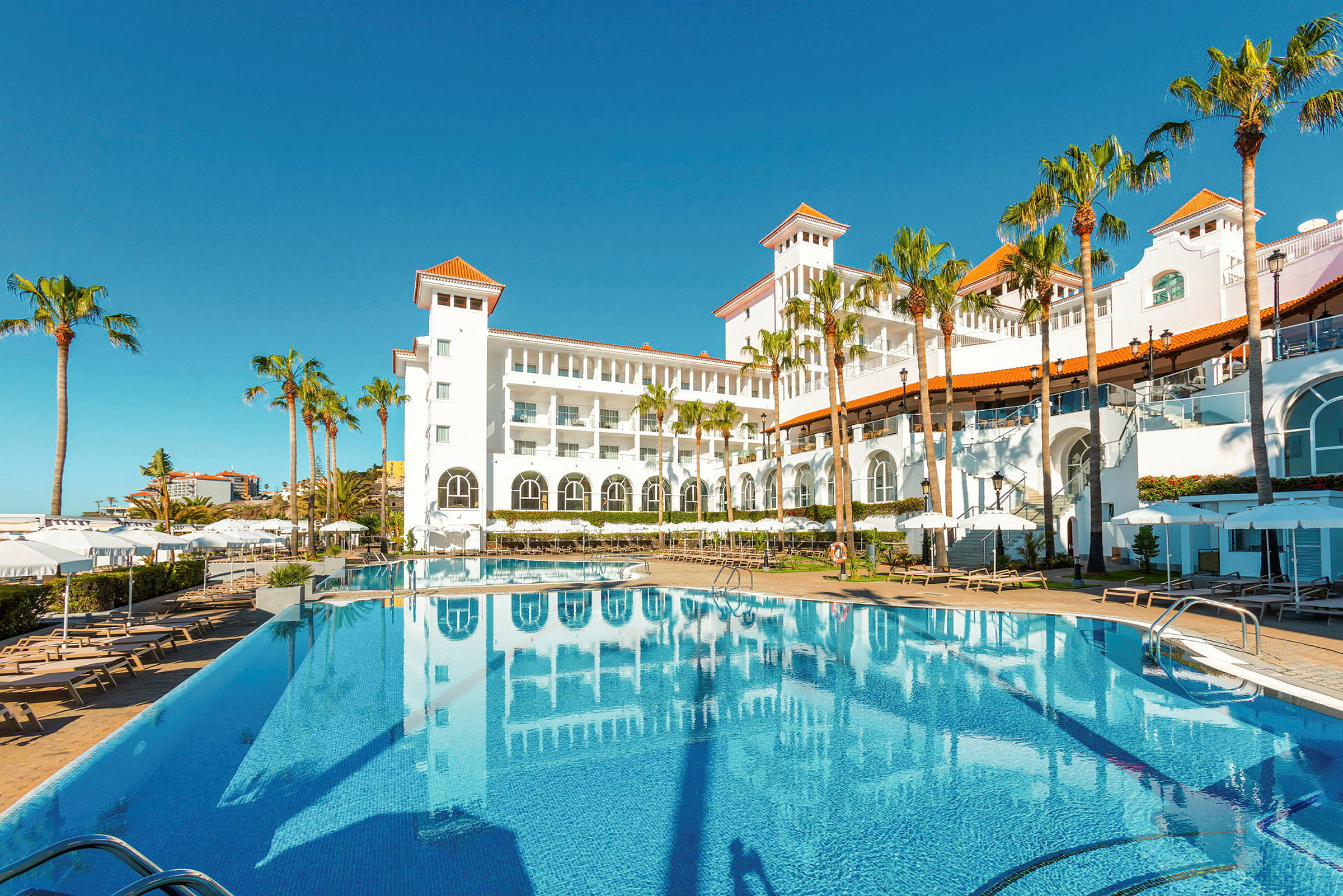 Hotell med vit fasad och pool i förgrunden. (AI-genererad text)