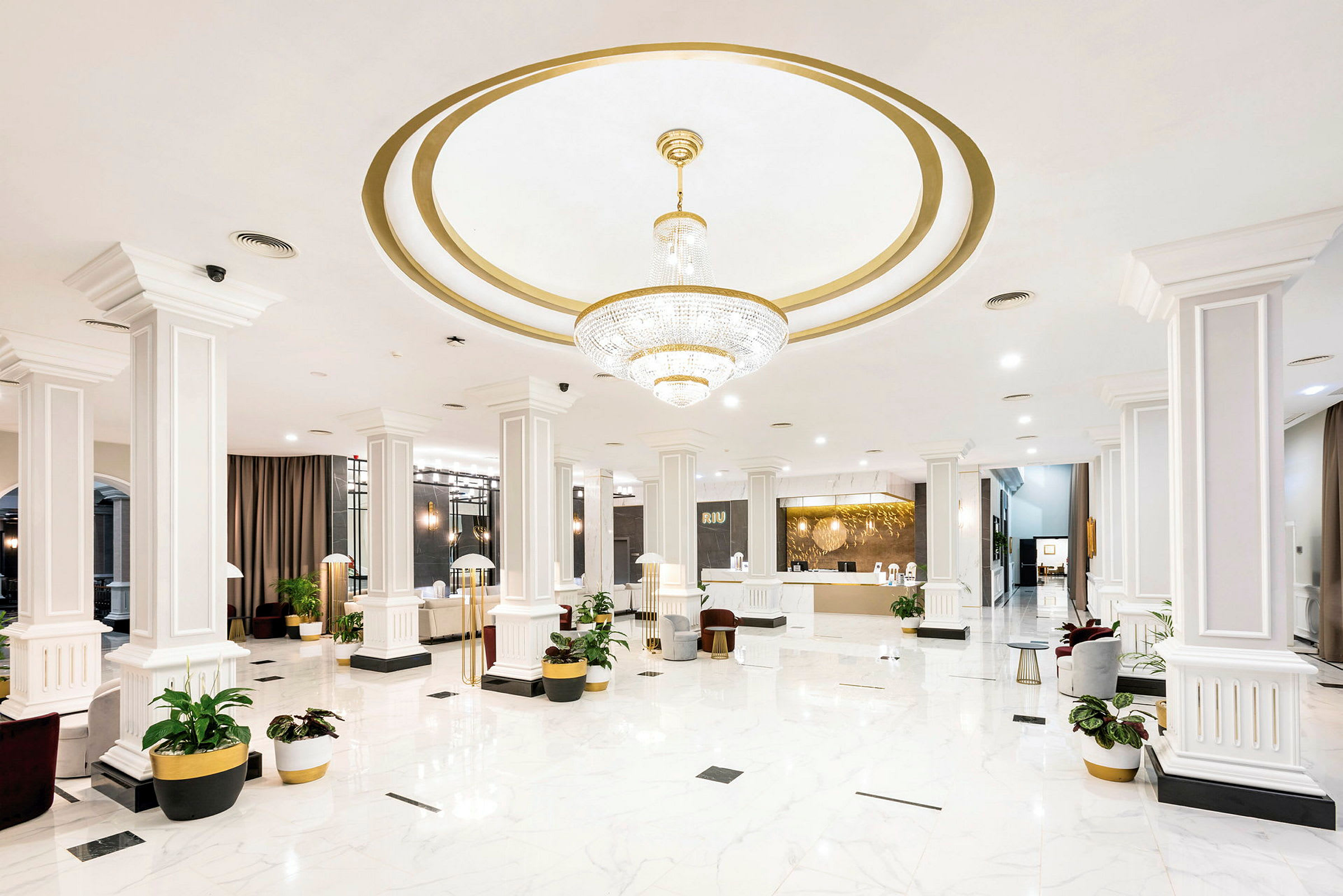 Hotellets lobby med vit marmorgolv, pelare och en stor ljuskrona. (AI-genererad text)
