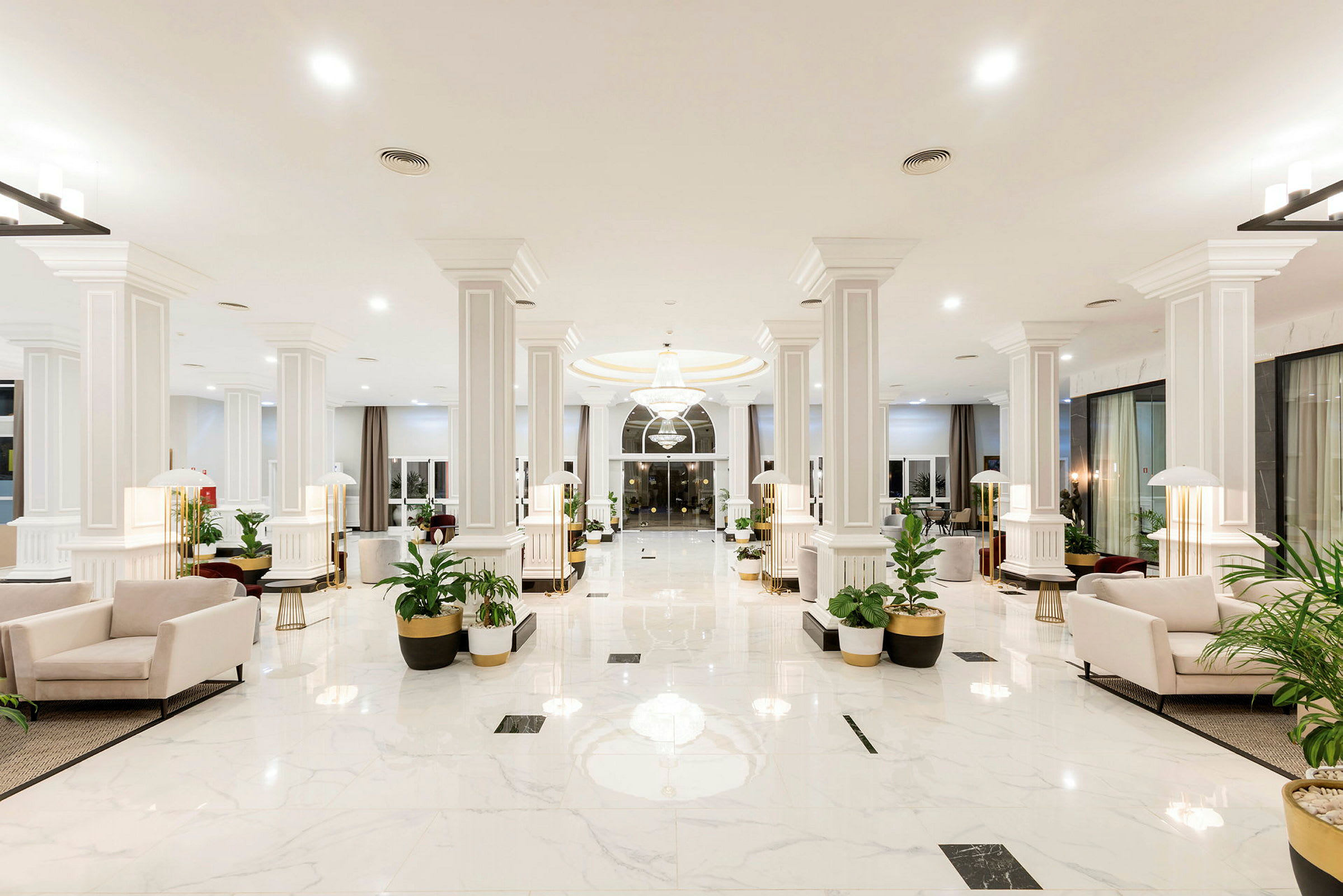 Ljus och rymlig hotellobby med vita marmorgolv, ljusa sittgrupper och gröna växter. (AI-genererad text)
