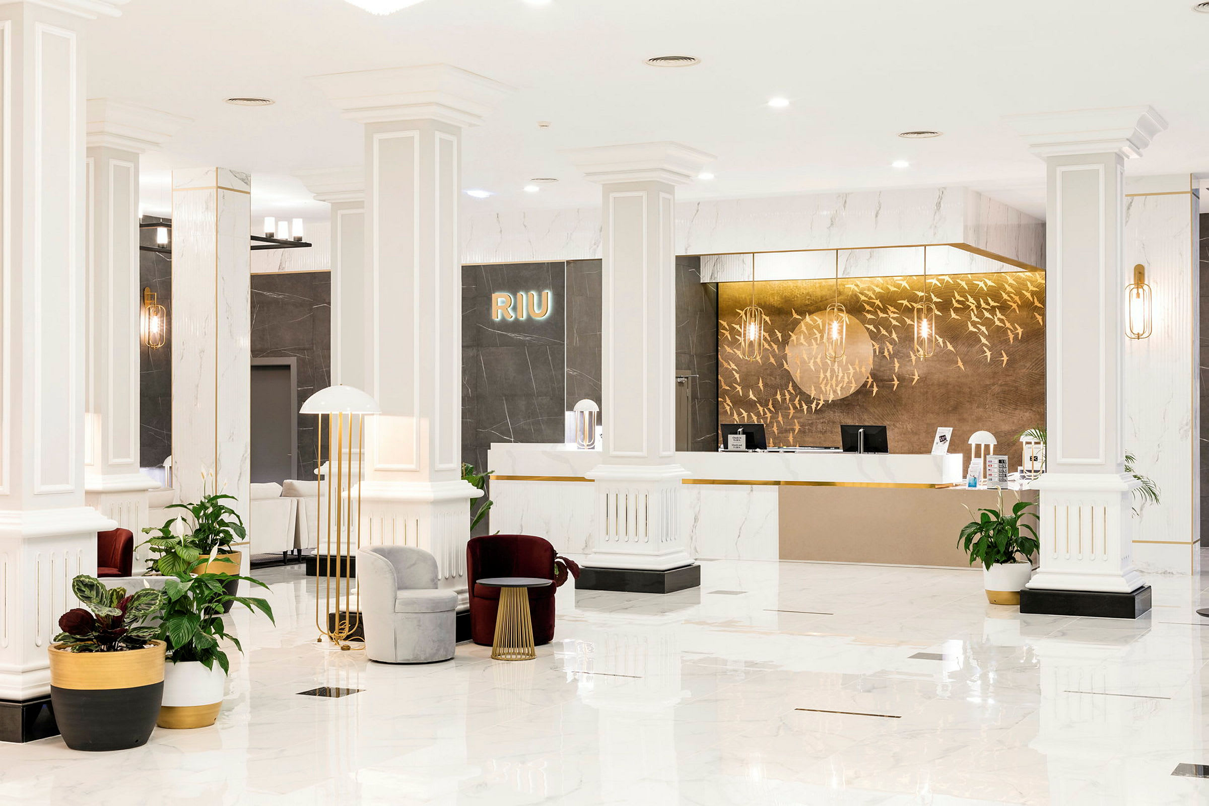 Receptionen på en Riu-hotell, modernt inredd med vita pelare, golv i ljus marmor, och eleganta möbler. (AI-genererad text)