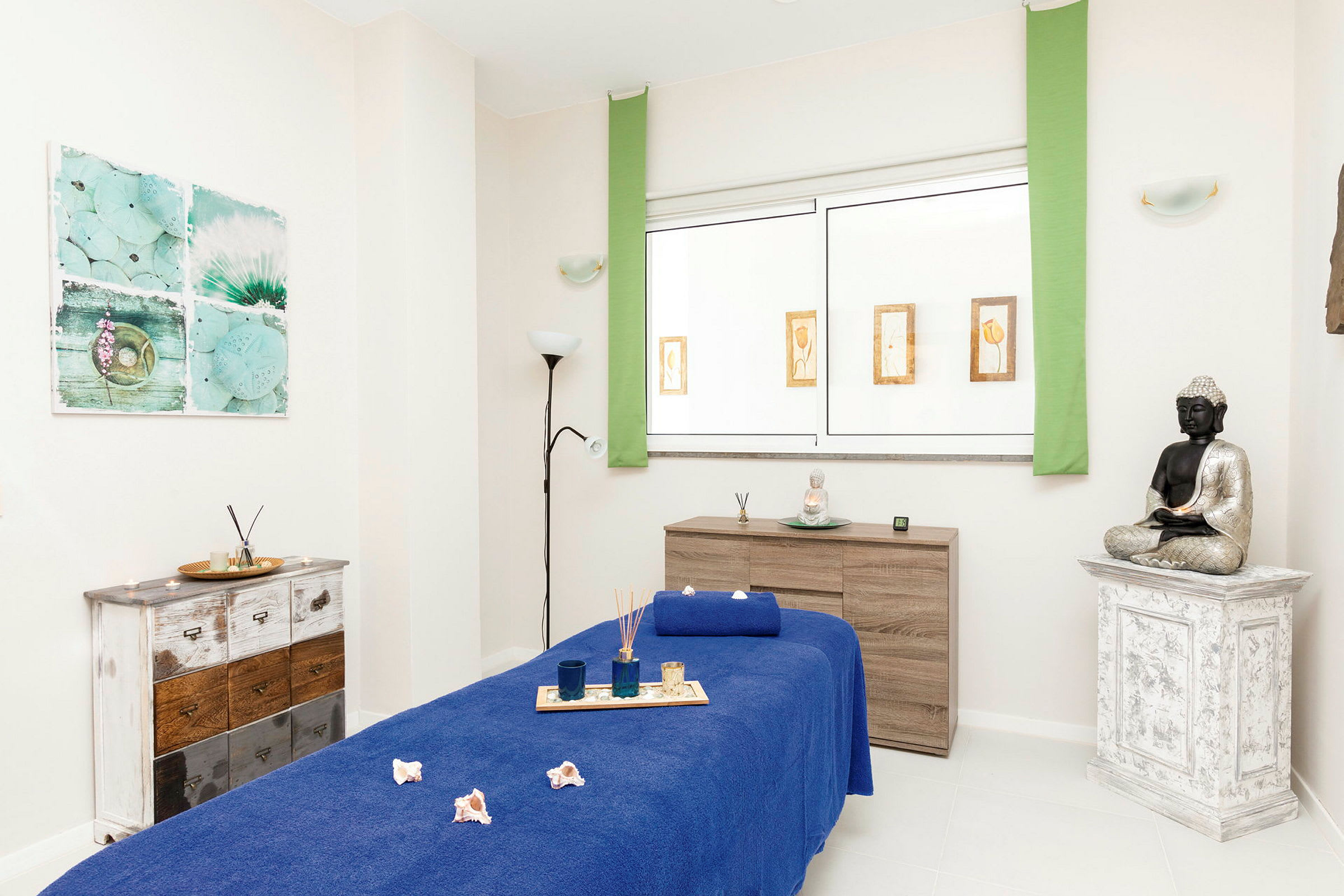 Ett behandlingsrum med blått täcke på massagebänk och dekor med Buddha-staty. (AI-genererad text)