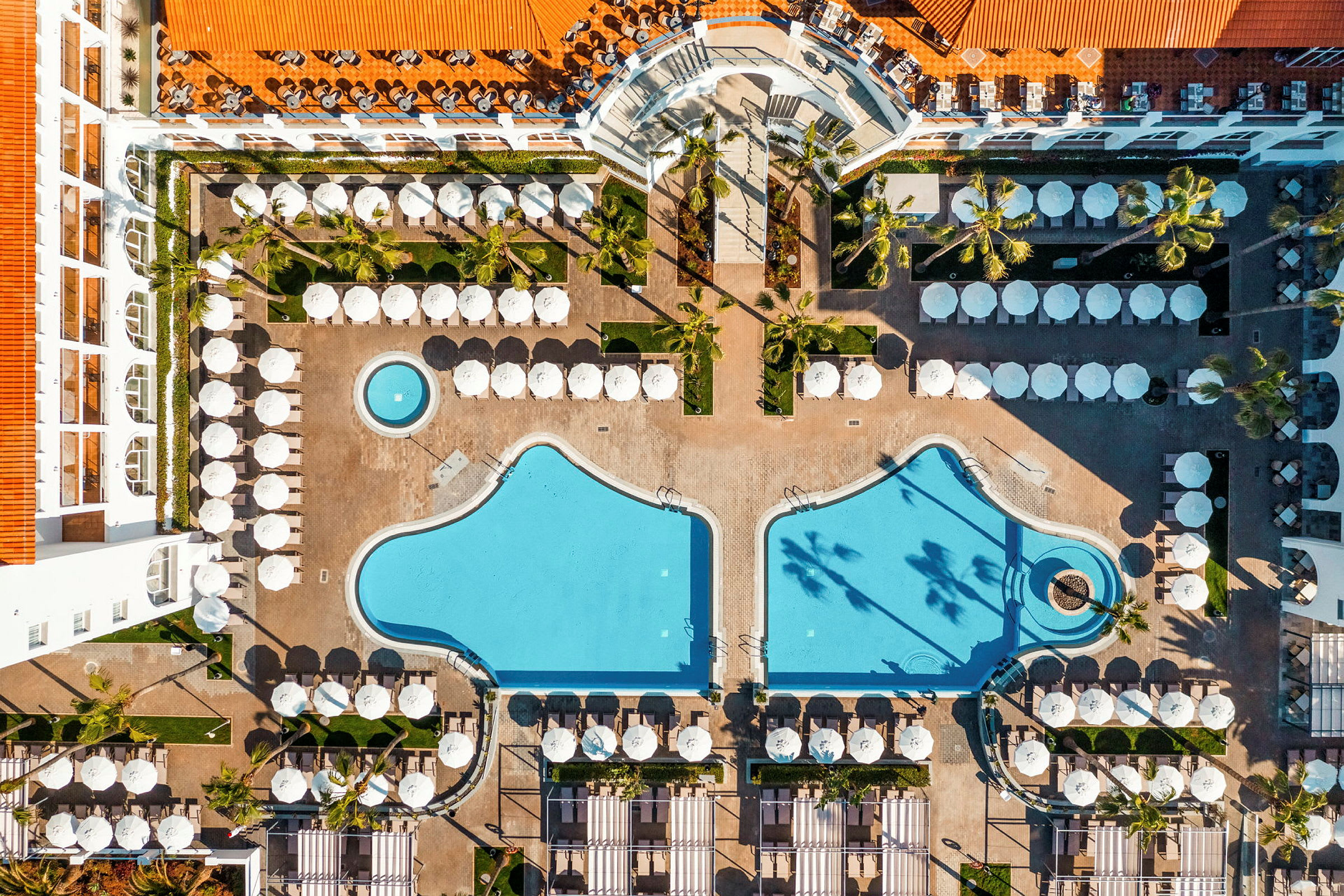Flygbild av hotellområde med två pooler och solstolar. (AI-genererad text)