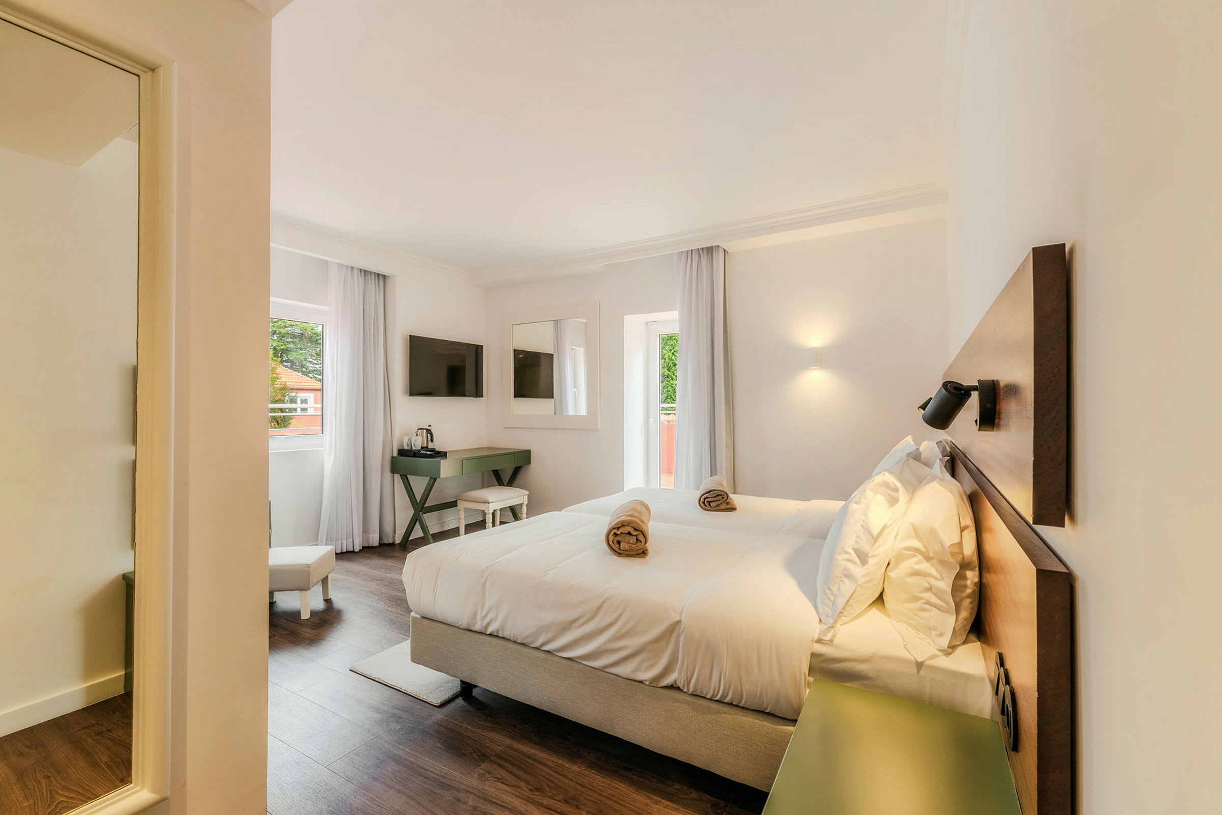 Ett ljust hotellrum med en dubbelsäng, ett fönster med gardiner, en TV på väggen och ett skrivbord. (AI-genererad text)