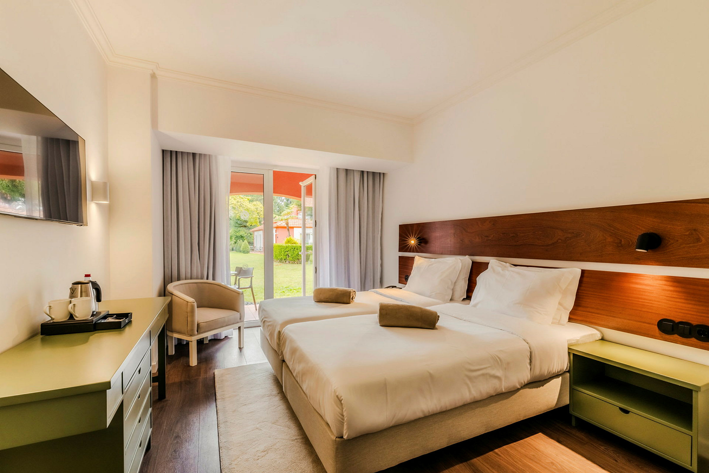 Hotellrum med två sängar som vetter mot en fönsterdörr som leder till en grönskande trädgård. (AI-genererad text)