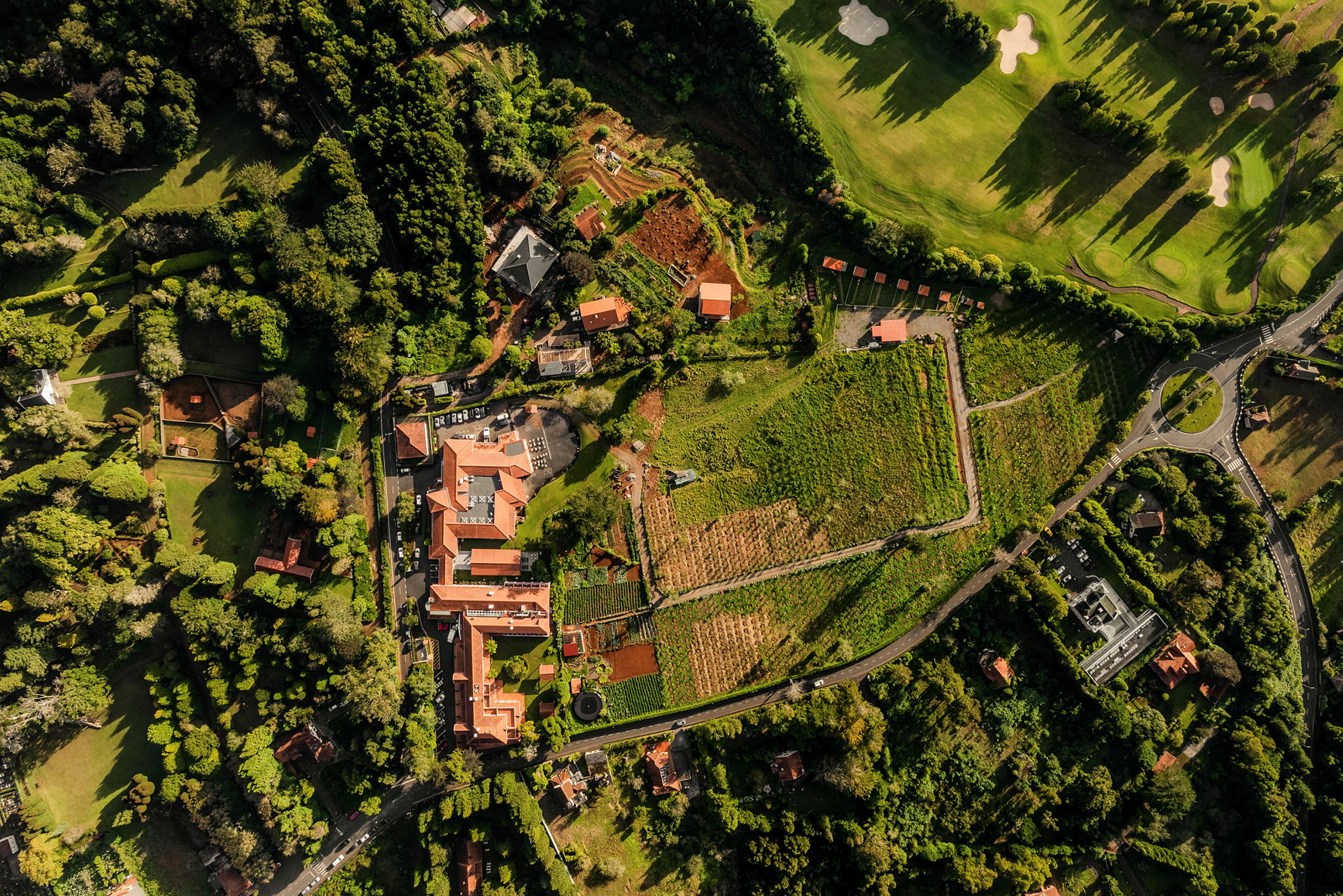 Flygfoto av ett område med byggnader, vinodlingar och trädgårdar i en grönskande omgivning. (AI-genererad text)