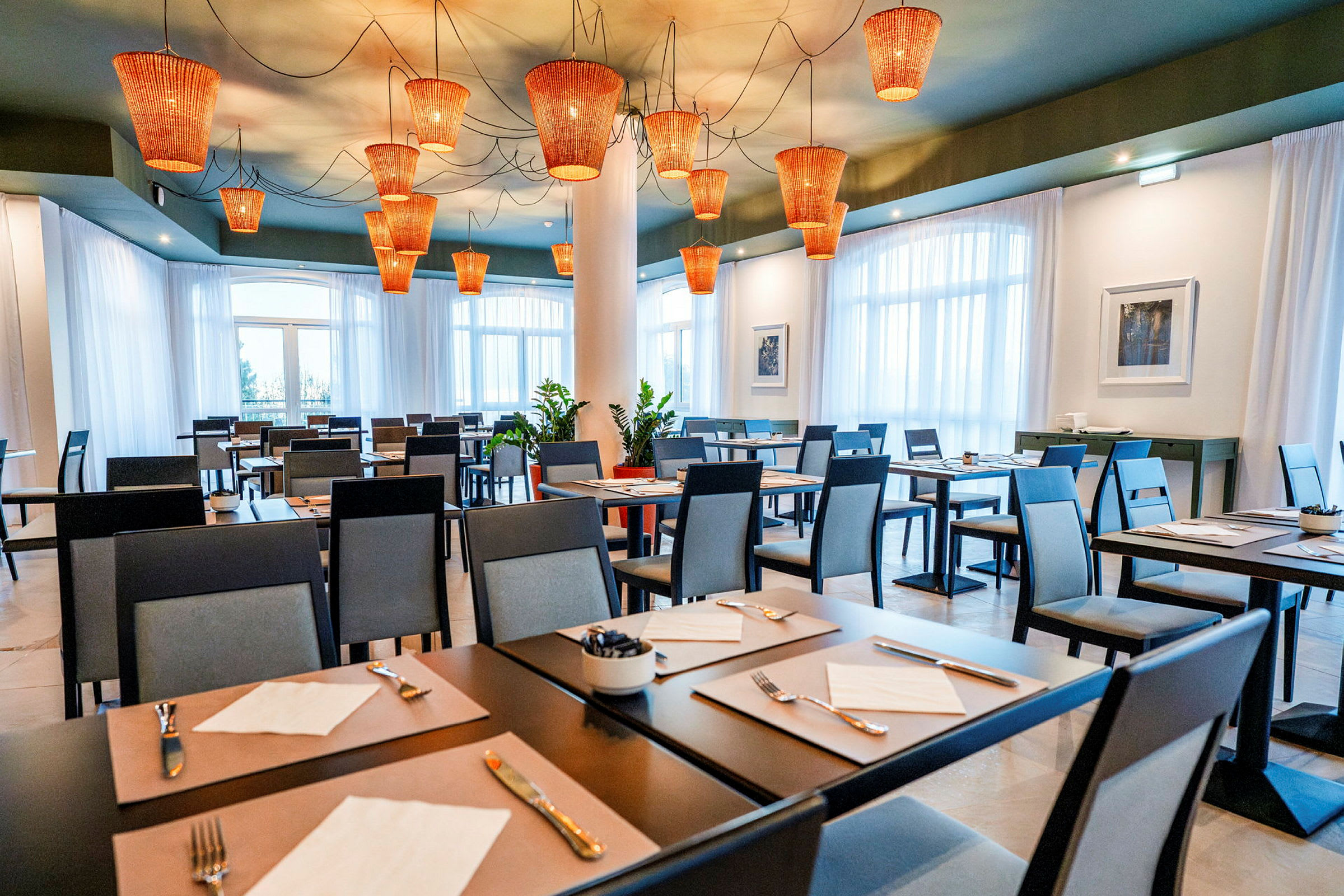Restaurang med dukade bord och moderna stolar, med orangefärgade lampor i taket. (AI-genererad text)