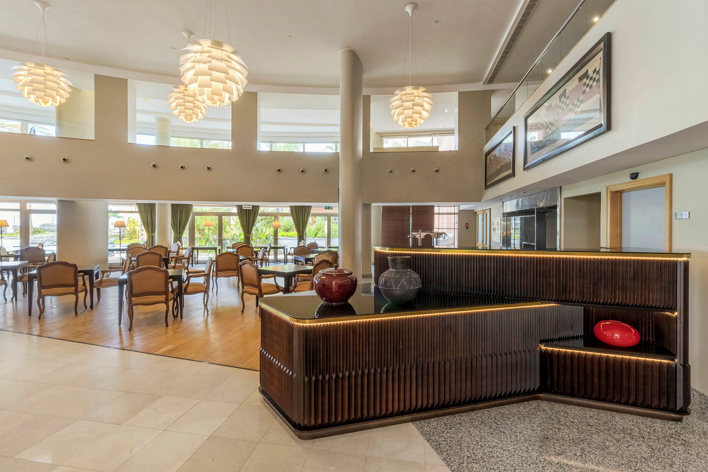 Ett elegant hotellobbyområde med bord och stolar samt dekorativa, moderna lampor. Receptionen har mörkt träpanel och dekorationer. (AI-genererad text)