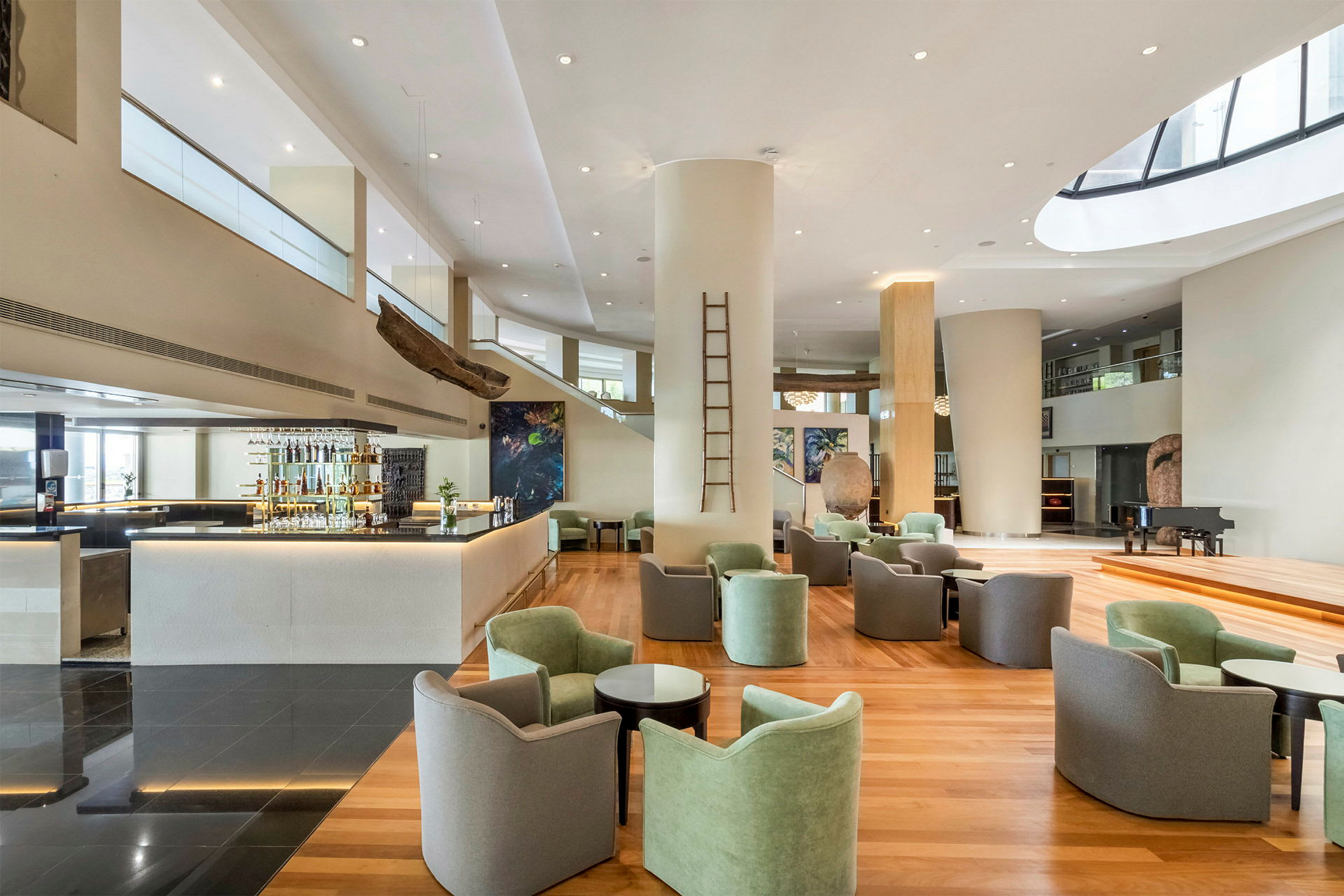 Ett modernt rum med en avslappnad lounge och barområde. Fåtöljer och bord är placerade på ett trägolv, medan en bar och unika konstverk syns i bakgrunden. (AI-genererad text)