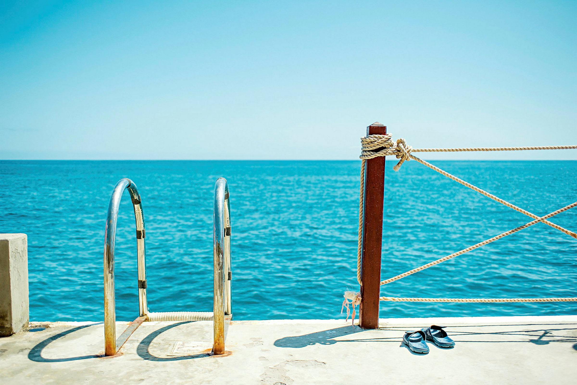 Metallstege och staket vid havskanten med sandaler på marken. (AI-genererad text)