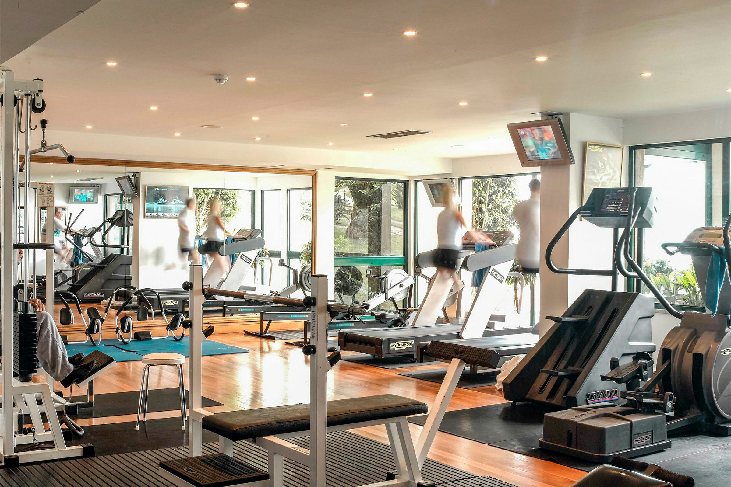 Bild på ett gym med olika träningsmaskiner och personer som tränar. (AI-genererad text)