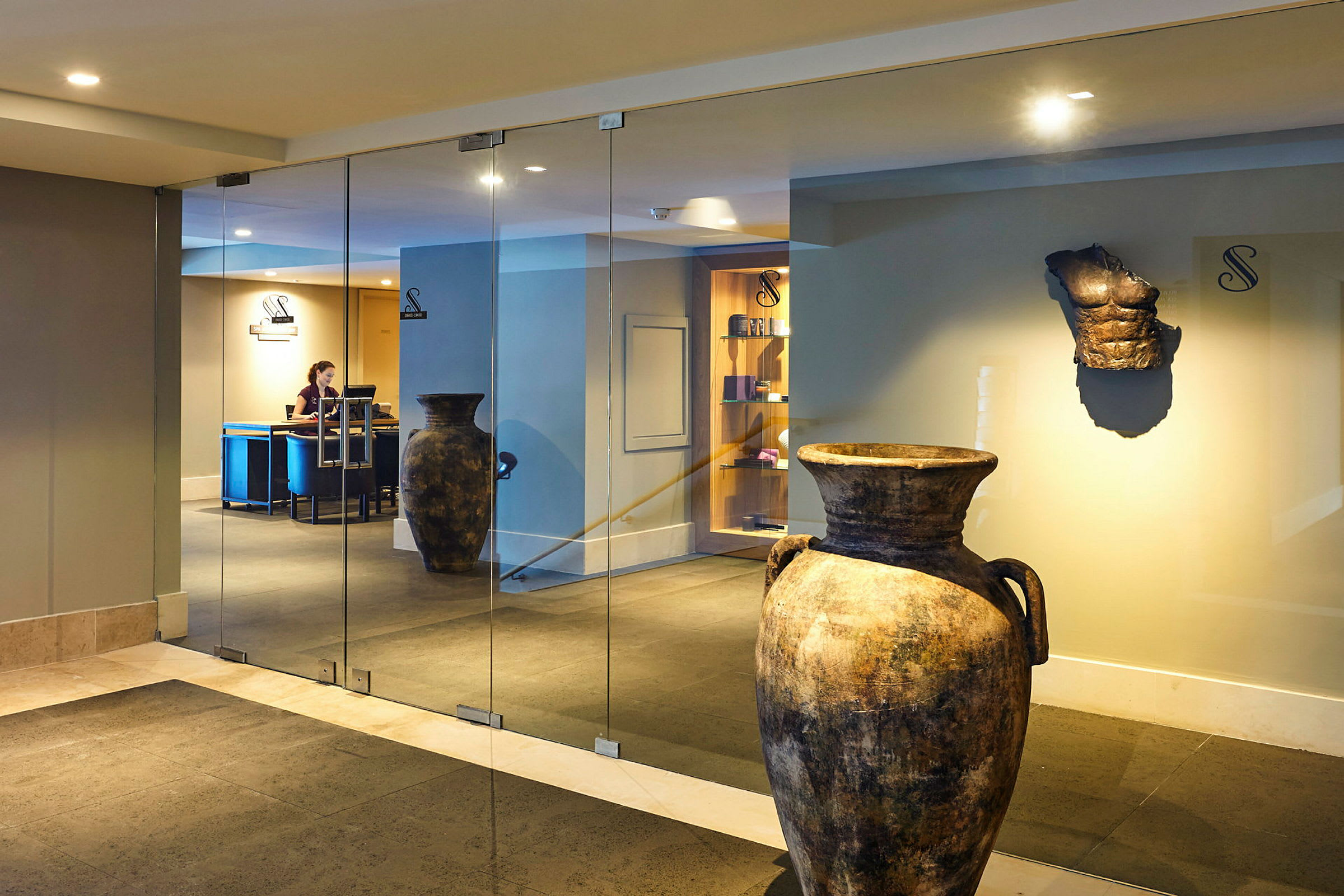 Keramikkrukor och en antik skulptur i en hotellobby med glasväggar. (AI-genererad text)