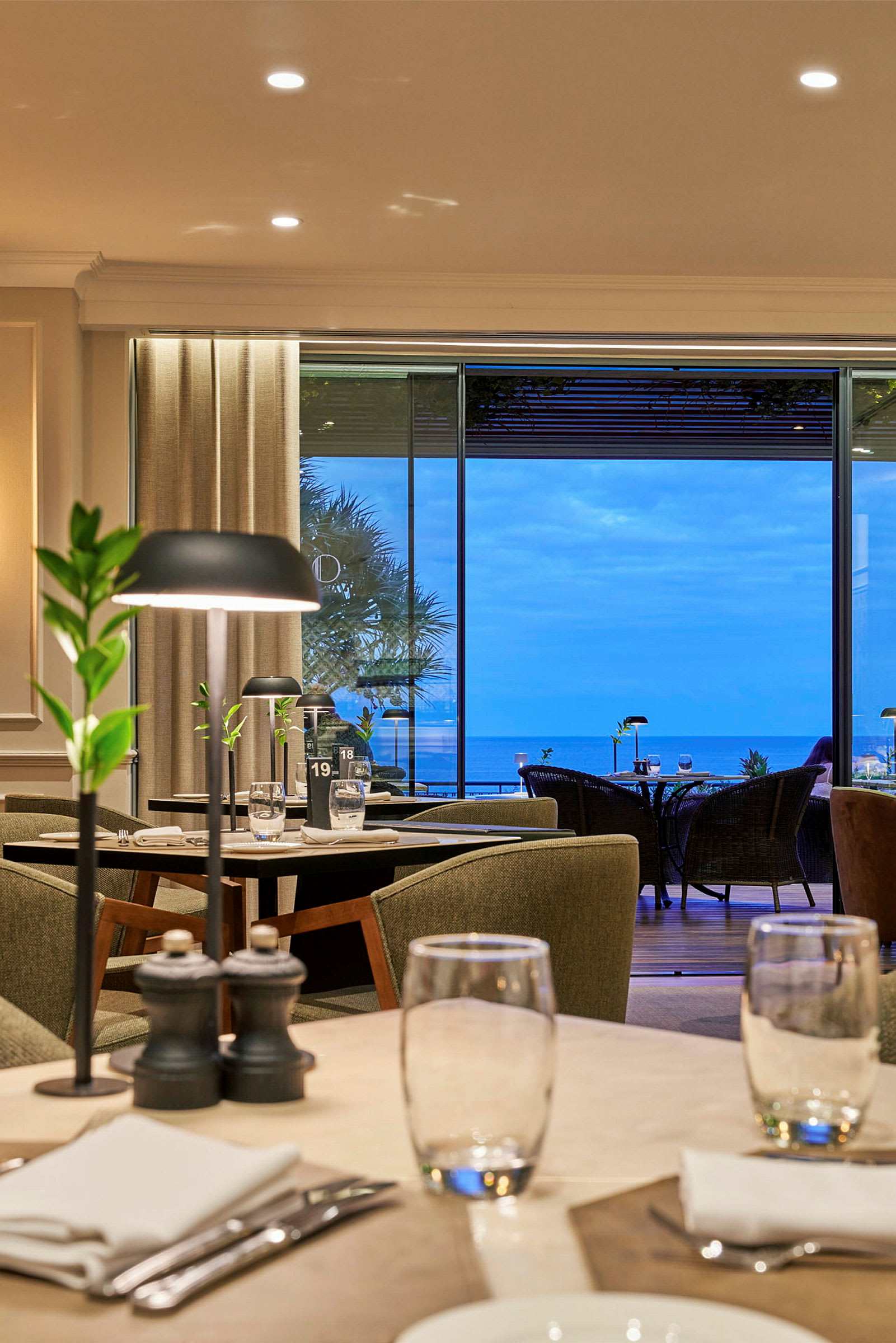 Interiör av en restaurang med dukade bord och utsikt över havet. (AI-genererad text)