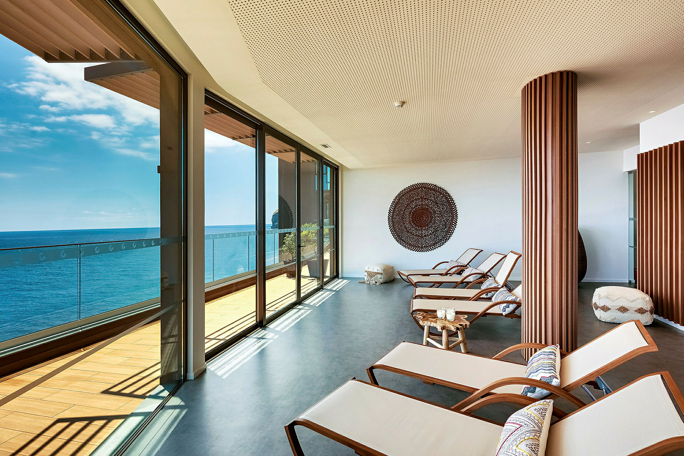 Utsikt över ett ljust rum med relaxstolar och panoramafönster mot havet. (AI-genererad text)
