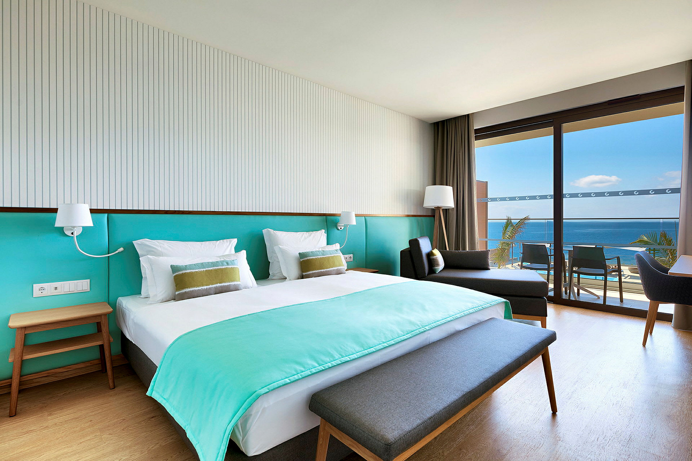 Ett hotellrum med en dubbelsäng, en sittmöbel och en balkong med utsikt över havet. (AI-genererad text)