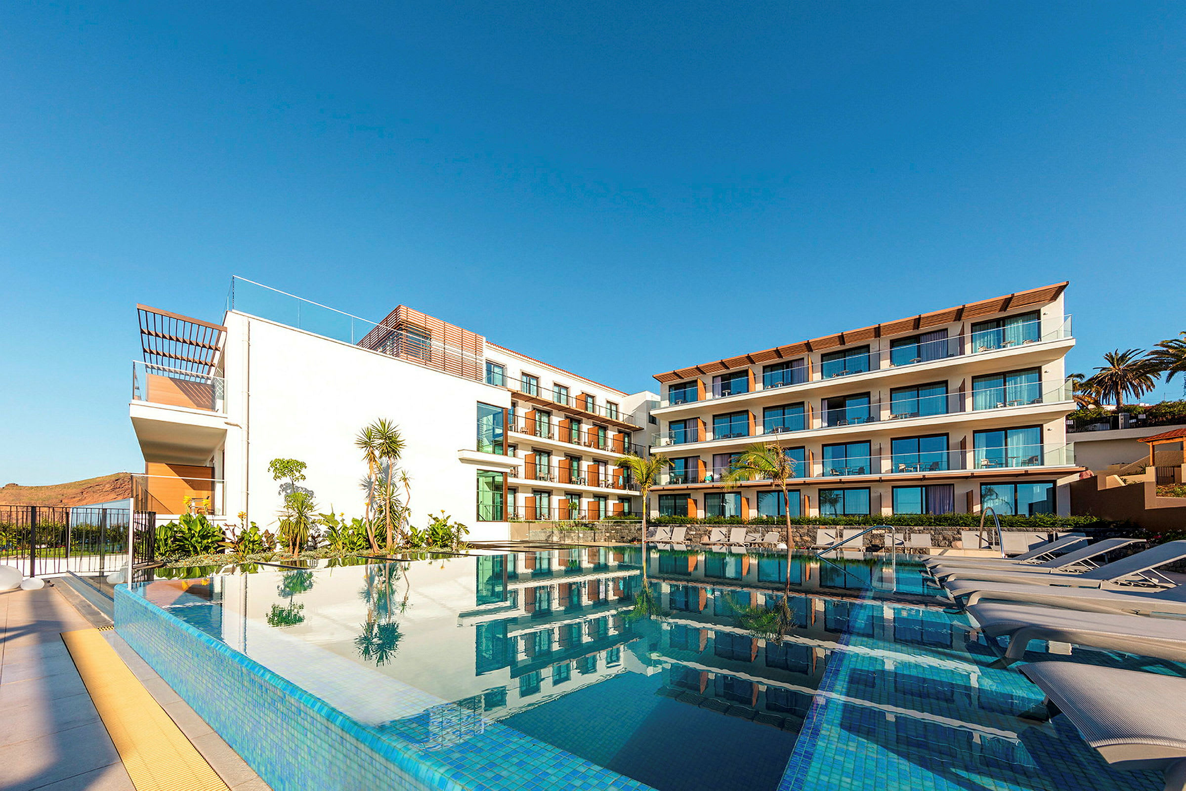 En modern hotellbyggnad med stora fönster och en pool i förgrunden. (AI-genererad text)