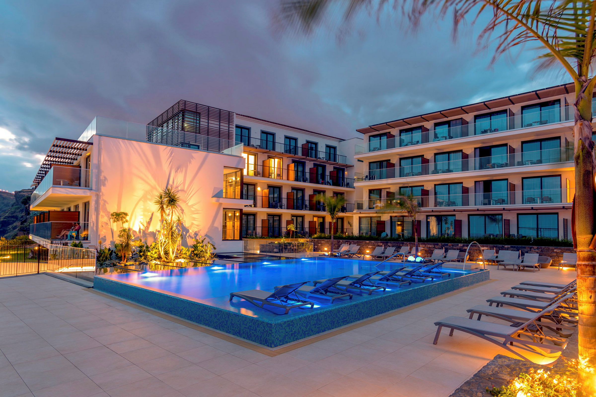 En nattvy av ett hotell med en upplyst pool framför byggnaden. (AI-genererad text)