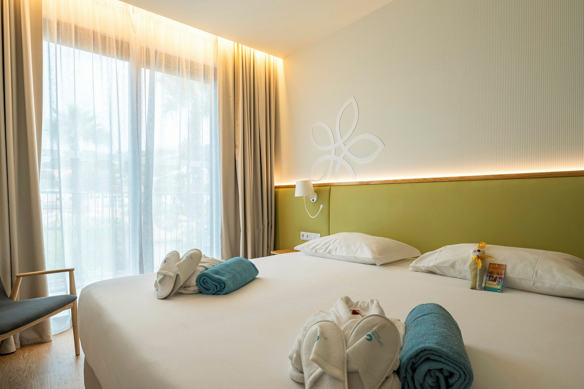 Hotellrum med en stor säng, ljus inredning och ett fönster med tunna gardiner. (AI-genererad text)