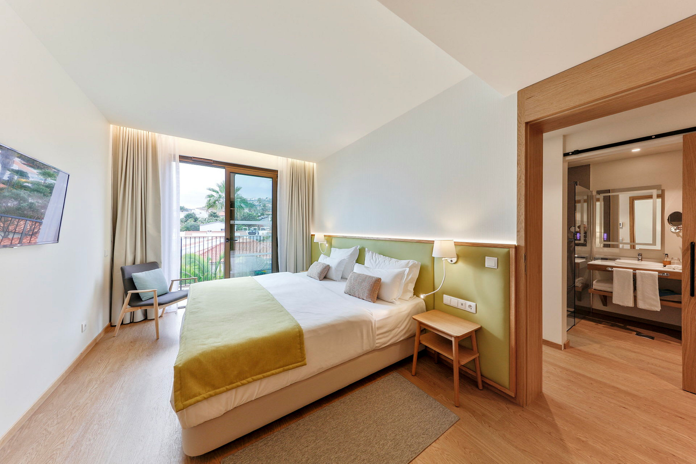 Ett hotellrum med en dubbelsäng, en fåtölj och ett öppet badrum. (AI-genererad text)