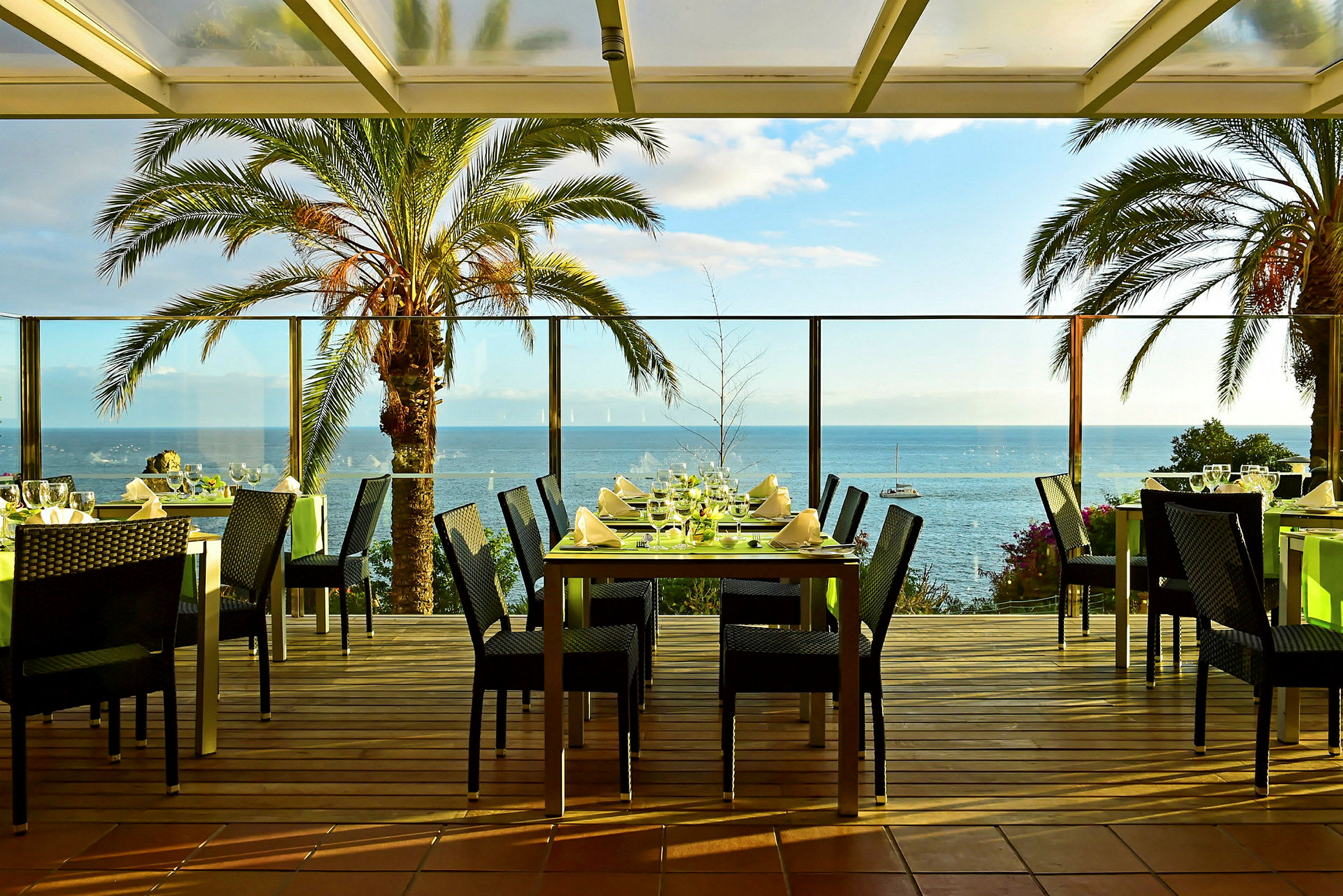 Restaurangbord på en terrass med utsikt över havet och palmer. (AI-genererad text)