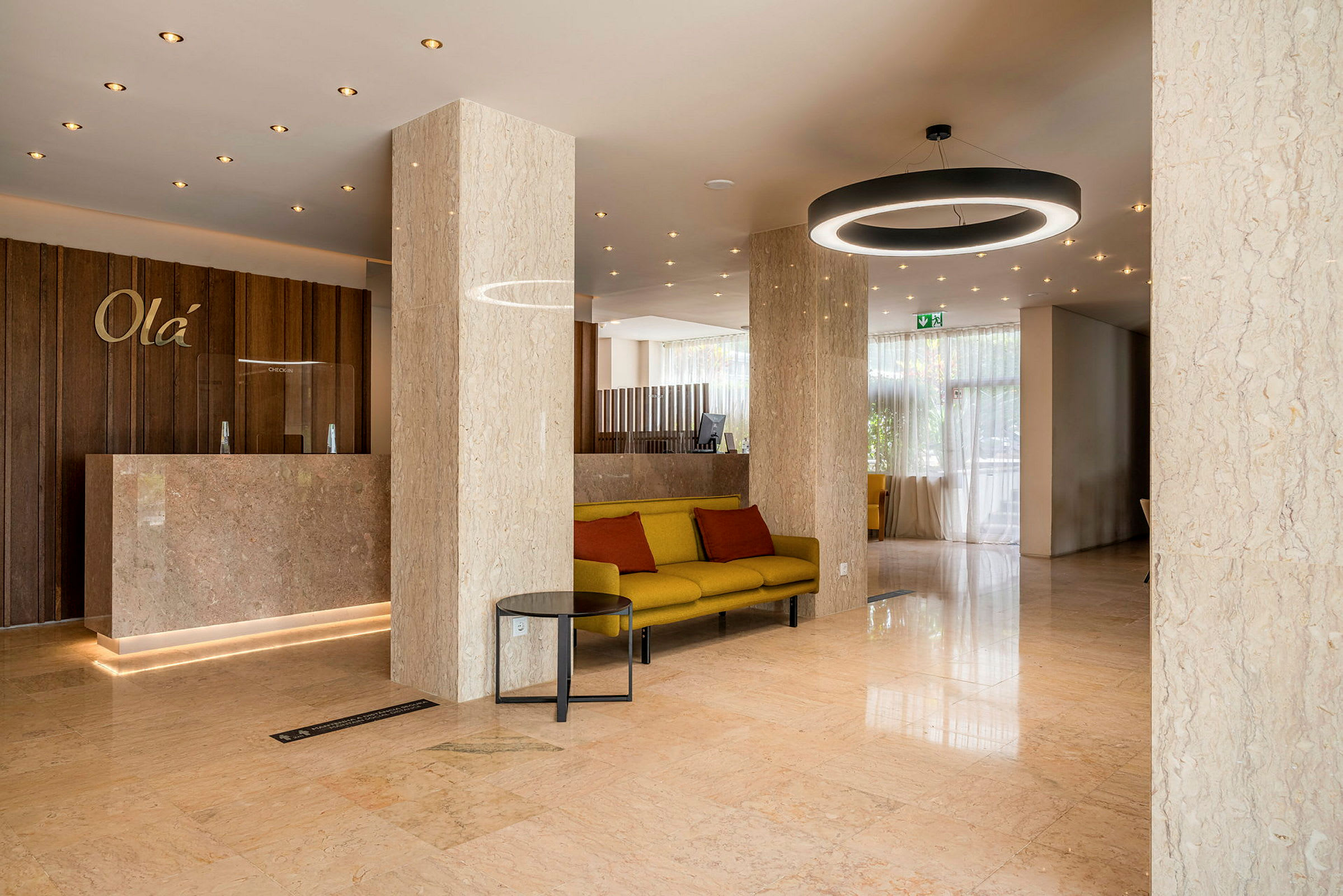 Hotellobby med marmorgolv och pelare, en reception med träpanel och en sittgrupp med gul soffa och röda kuddar. (AI-genererad text)