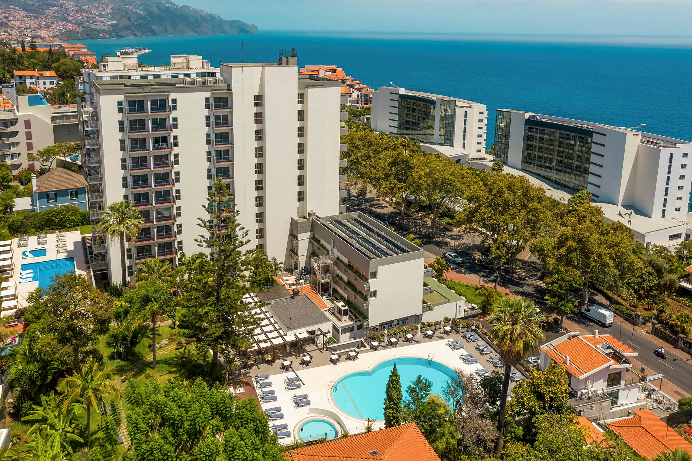 Hotellbyggnad med pool och omgivande grönska, hav i bakgrunden. (AI-genererad text)