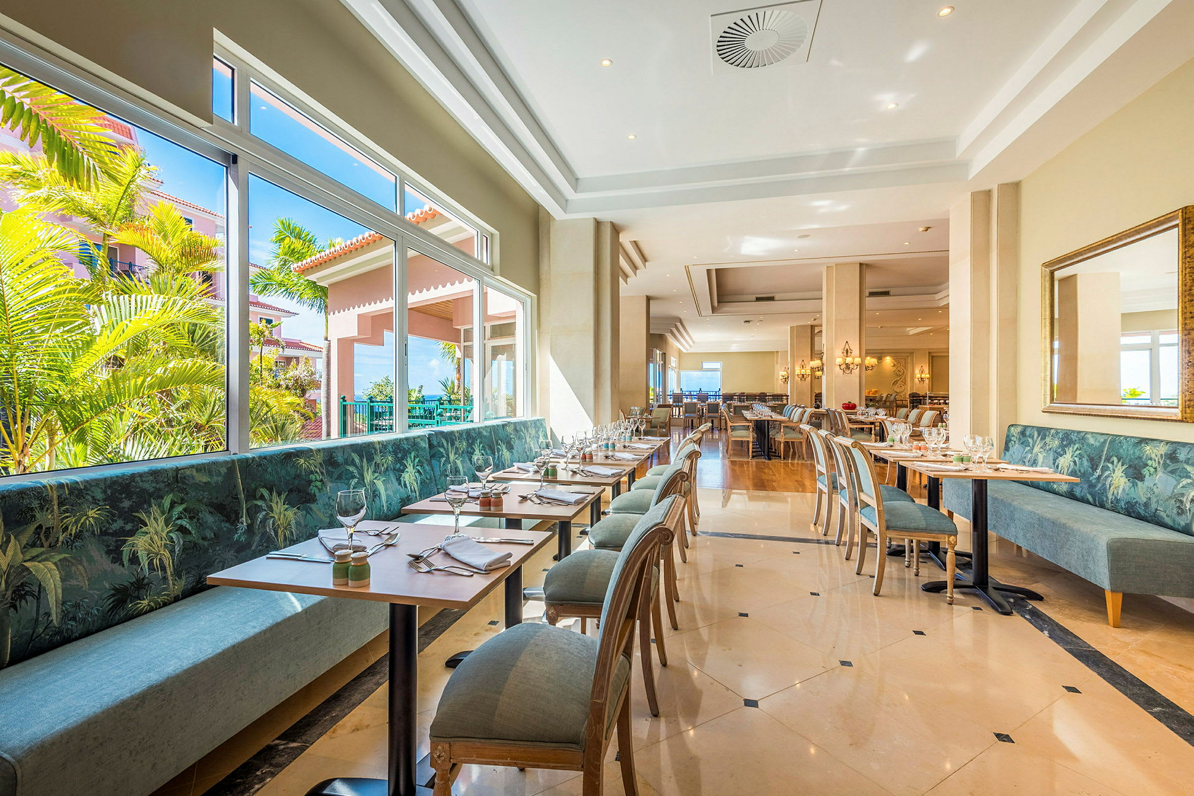 En ljus restaurang med moderna bord och stolar samt stora fönster med utsikt över grönska. (AI-genererad text)