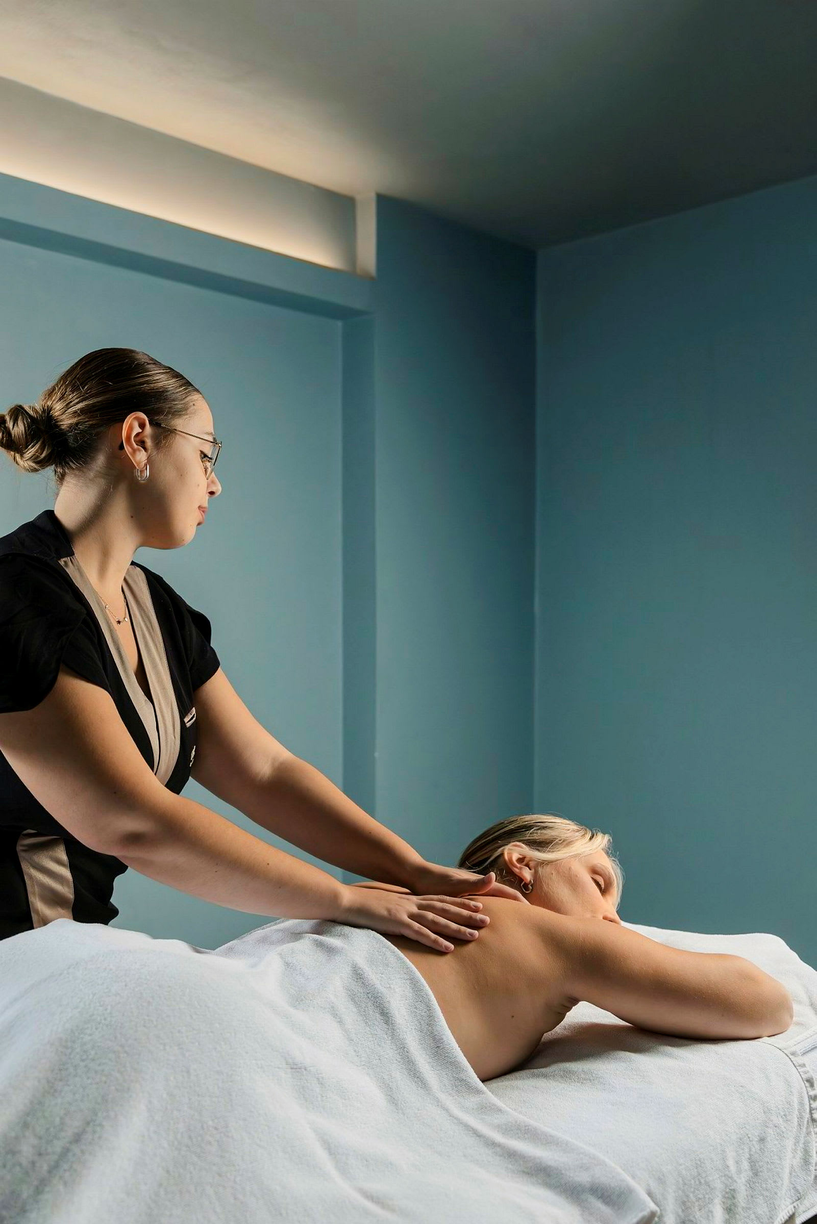 En person får en ryggmassage av en massageterapeut i ett rum med blå väggar. (AI-genererad text)