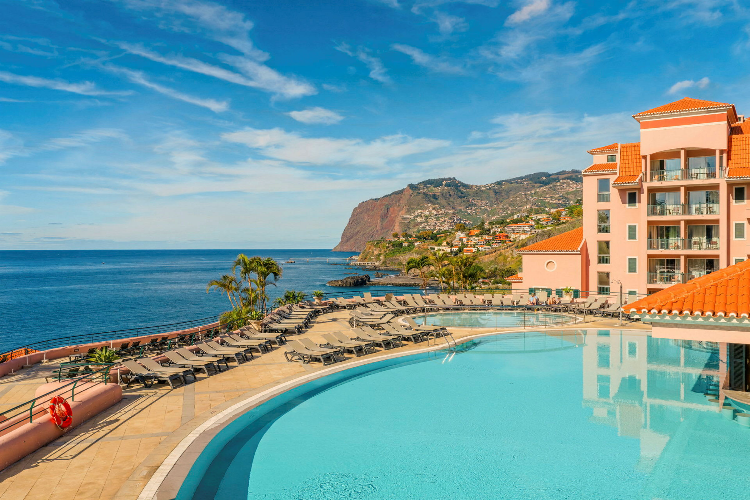 Bild av ett hotellkomplex med pool, solstolar och havsutsikt. (AI-genererad text)