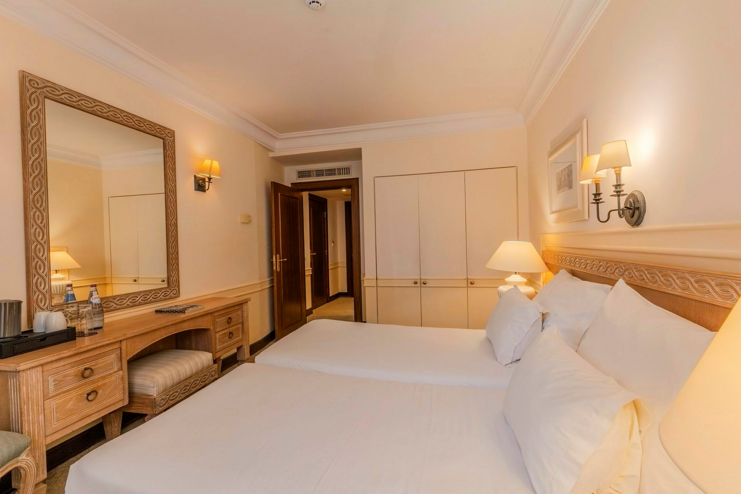 Ett hotellrum med två enkelsängar, ett skrivbord med spegel, garderob och dörr in till rummet. (AI-genererad text)