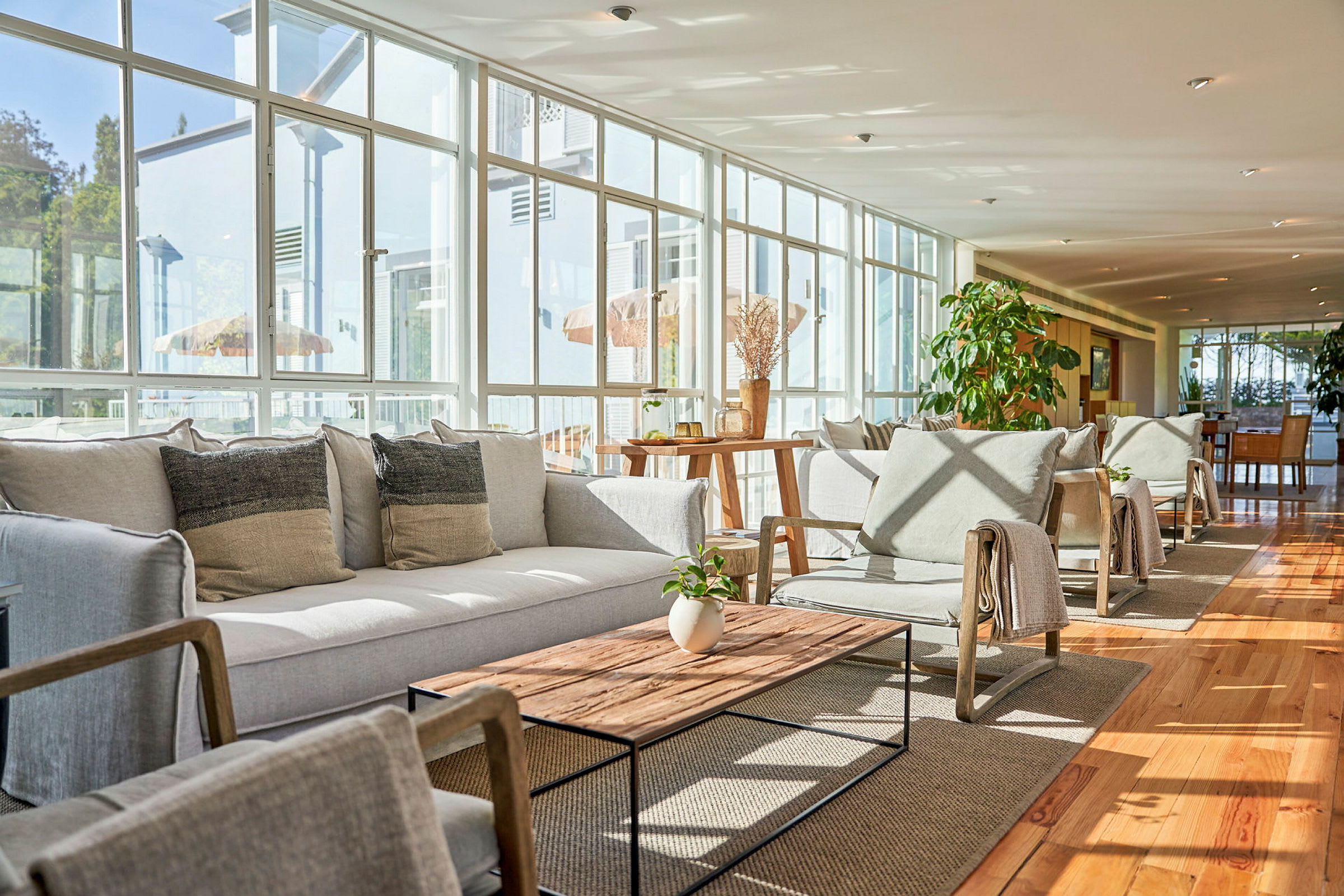 Ljus lounge med sittmöbler och soffbord, omgivna av stora fönster. (AI-genererad text)