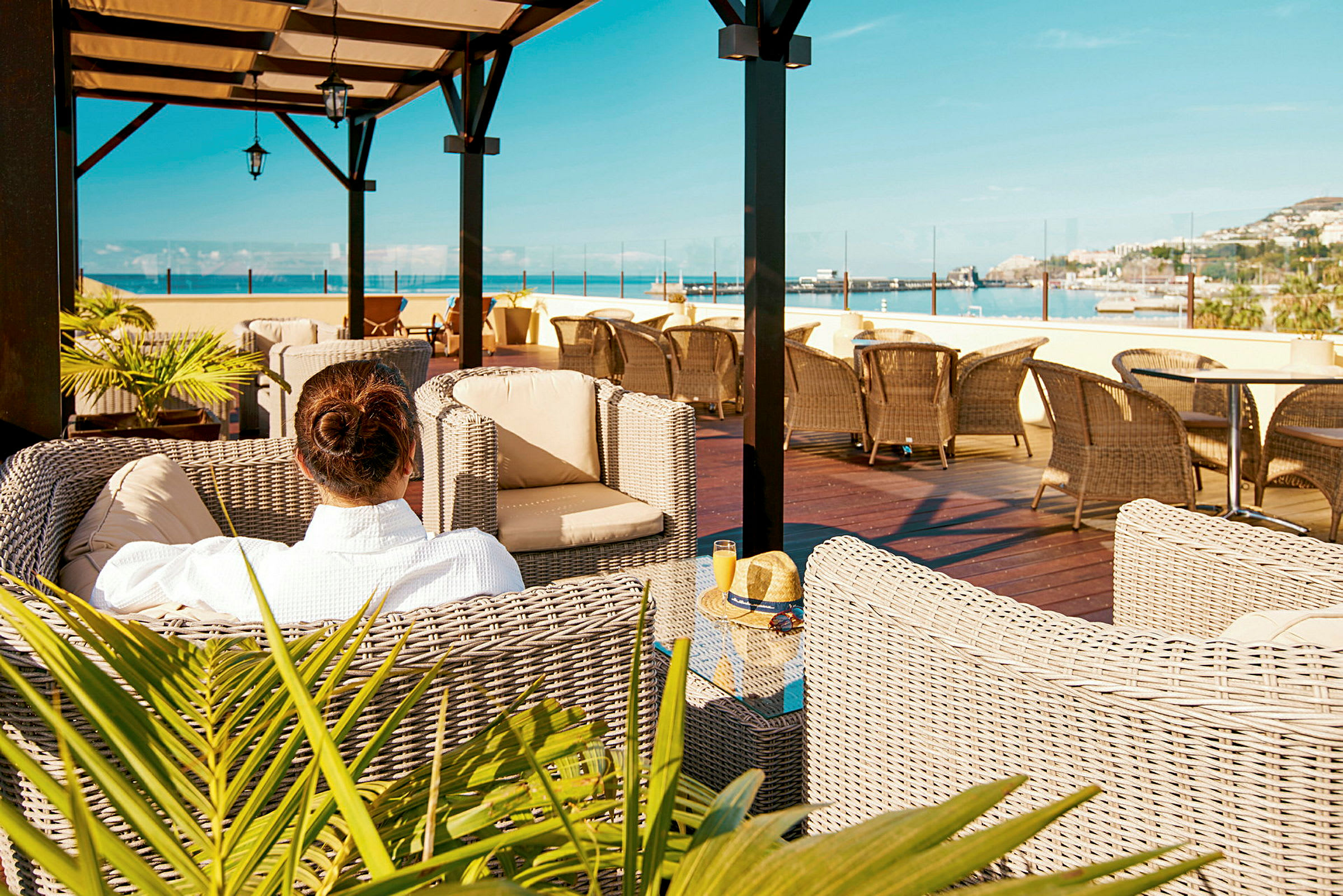En person sitter i en flätad fåtölj på en terrass med utsikt över havet. (AI-genererad text)