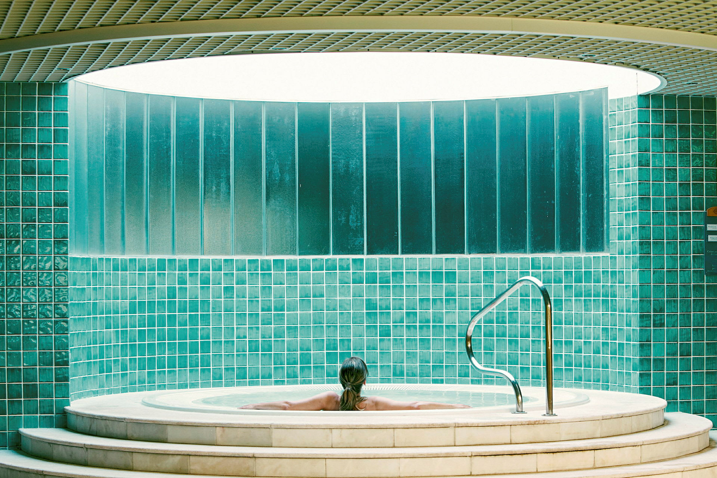Person som sitter i en bubbelpool omgiven av gröna kakelväggar. (AI-genererad text)
