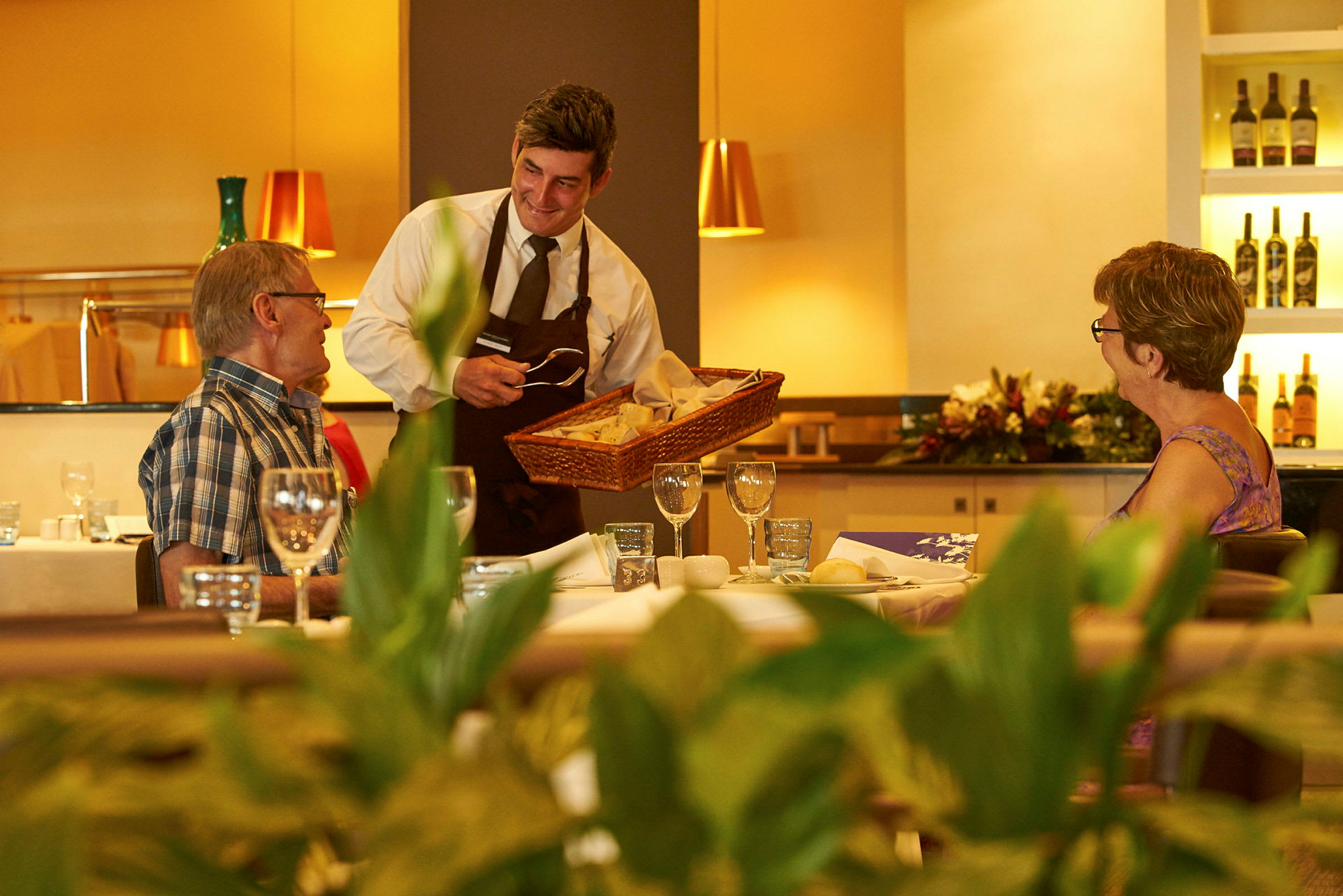 En servitör erbjuder bröd till gäster vid ett dukat bord på en restaurang. (AI-genererad text)