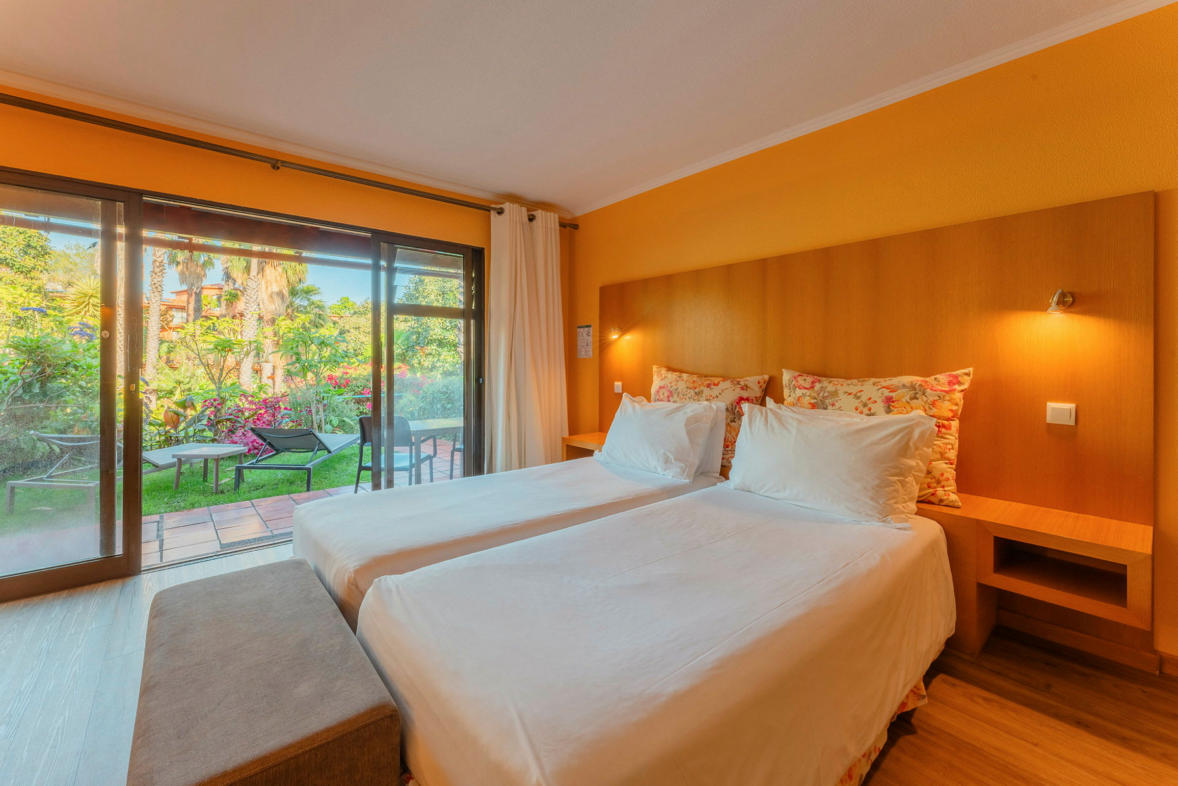 Ett hotellrum med två enkelsängar, mjuka kuddar och ett stort glasfönster som vetter mot en trädgård. (AI-genererad text)