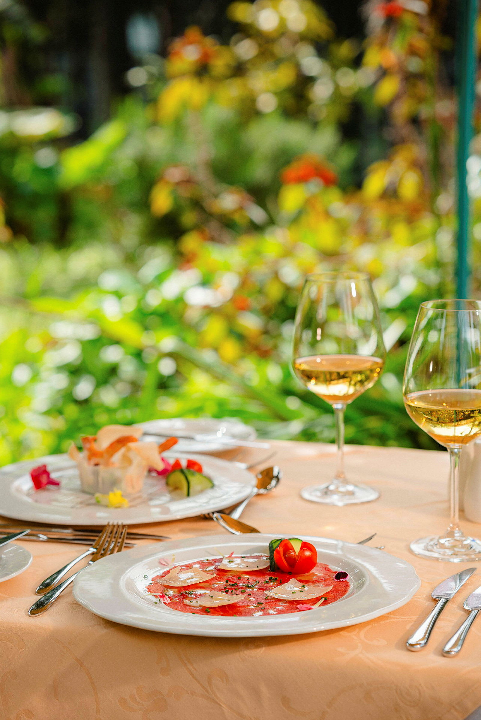 Två tallrikar med eleganta maträtter med två glas vitt vin på ett bord utomhus. (AI-genererad text)