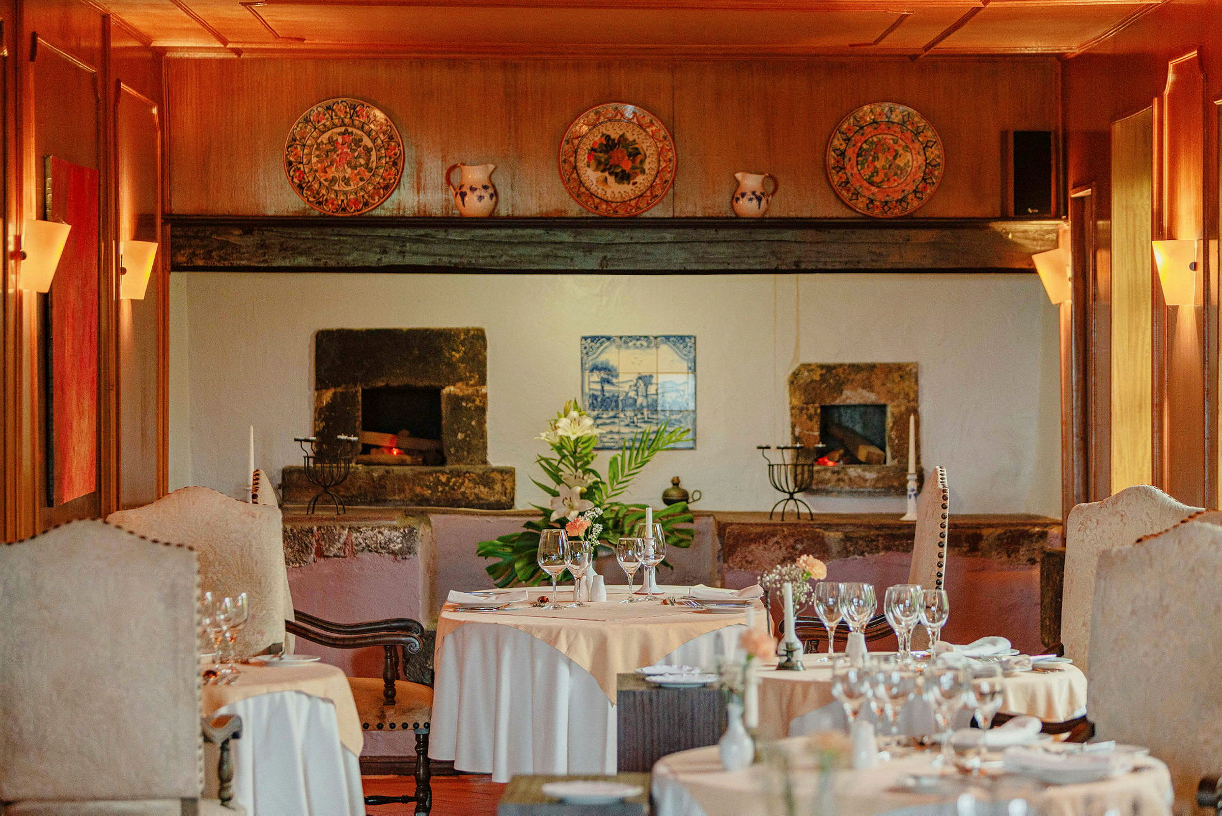 En restaurang med dukade bord, eleganta stolar och en dekorativ vägg med en öppen spis. (AI-genererad text)