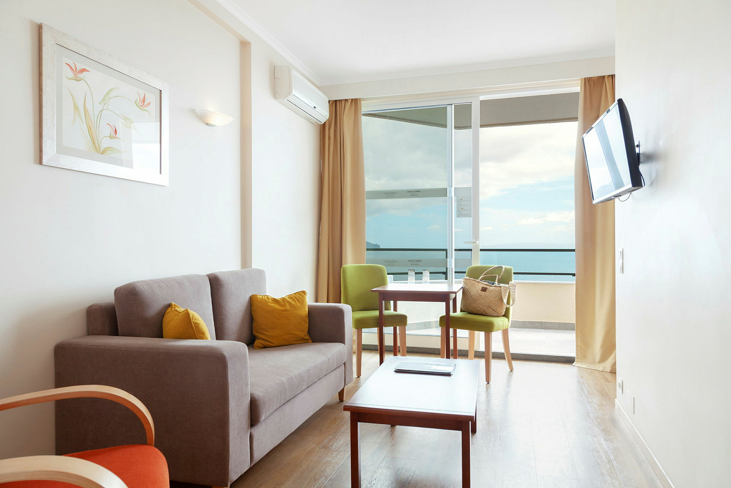 Ett vardagsrum med en soffa, två stolar, ett bord och en stor balkong med utsikt över havet. (AI-genererad text)