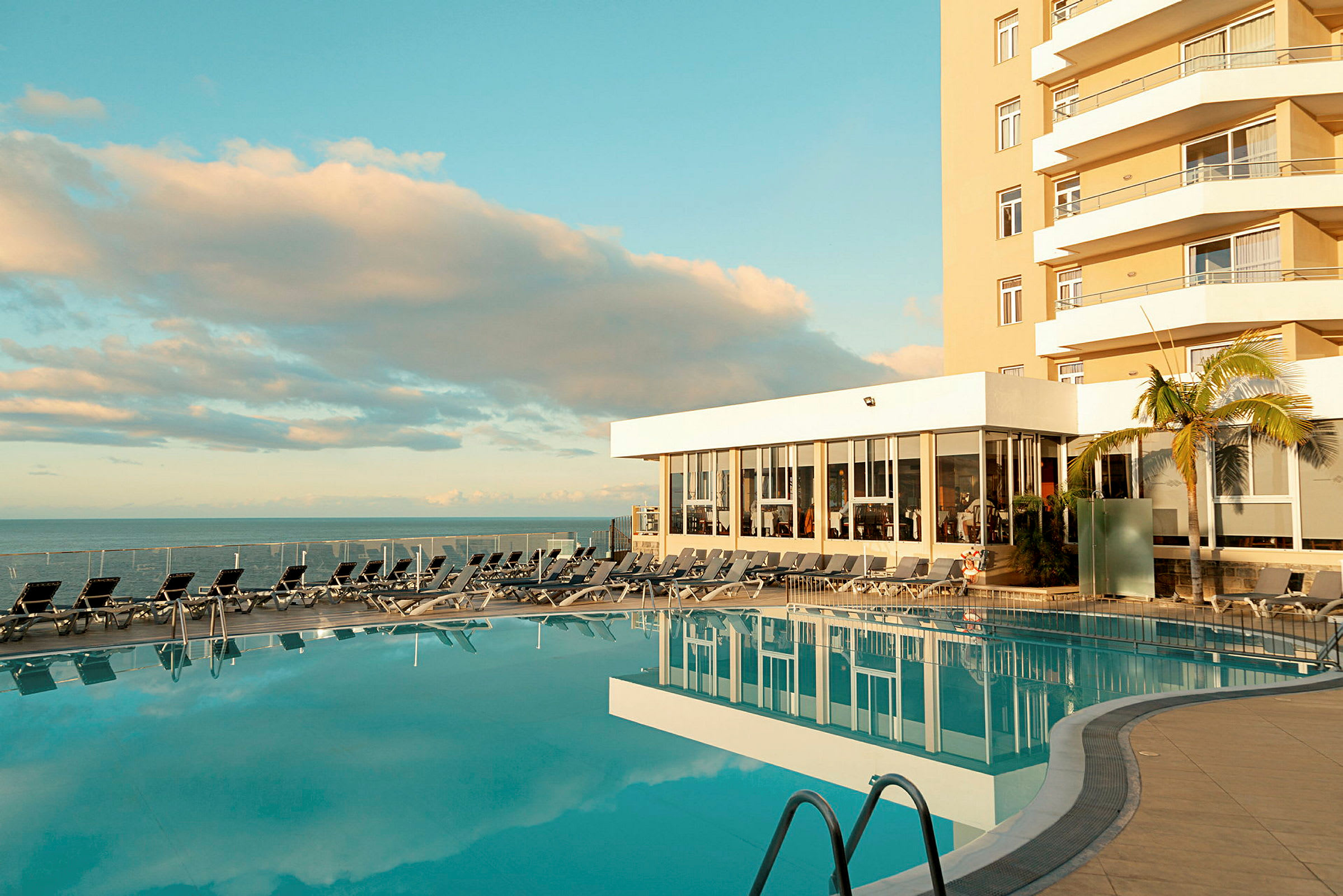 Utomhuspool vid hotell med solstolar och havsutsikt. (AI-genererad text)