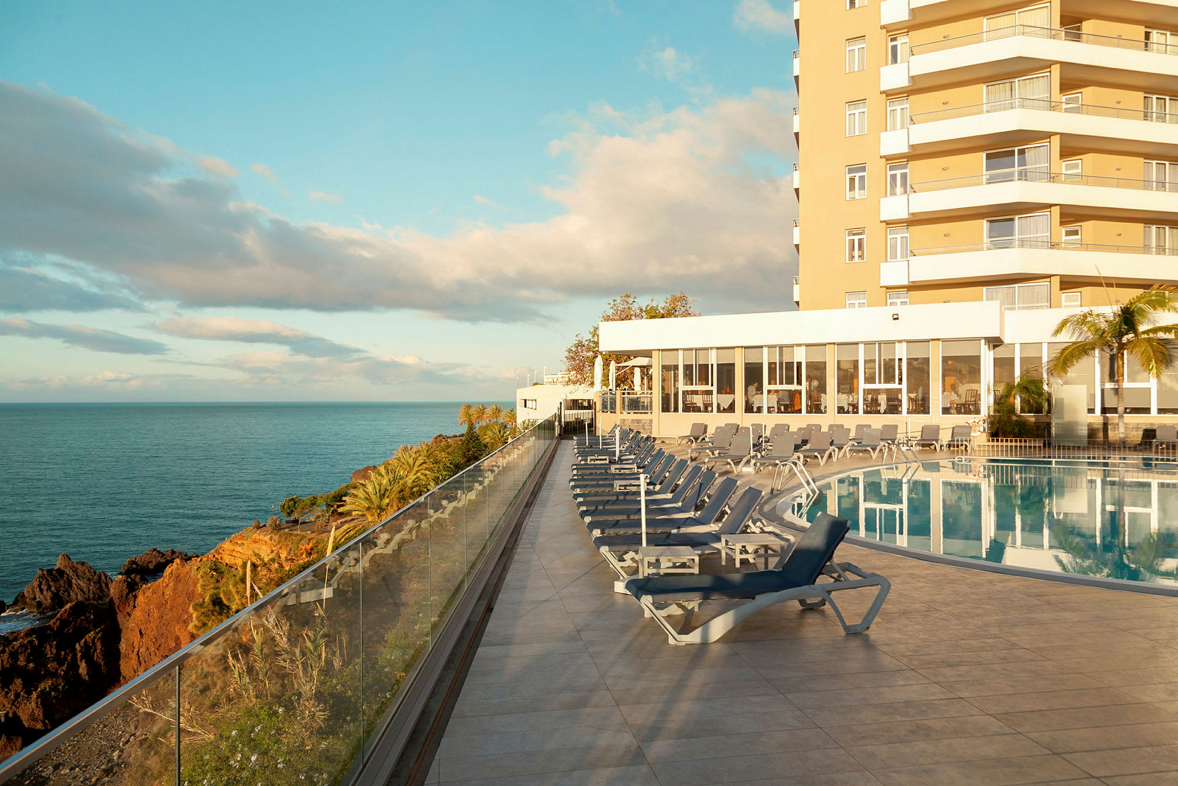 Utomhuspool med solstolar, havsutsikt och hotellbyggnaden i bakgrunden. (AI-genererad text)