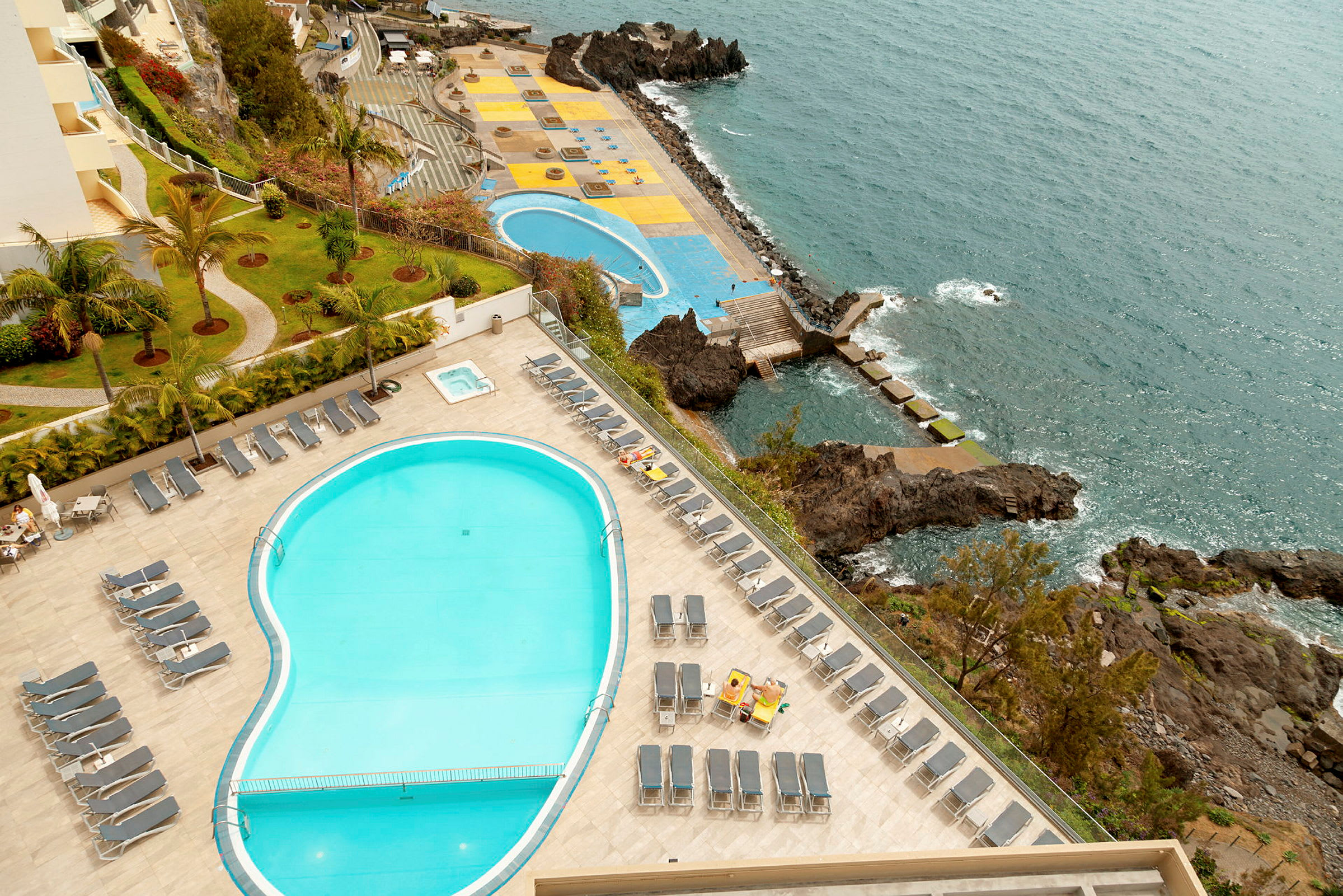 Hotellpoolområde med solstolar, havsutsikt och klippor. (AI-genererad text)