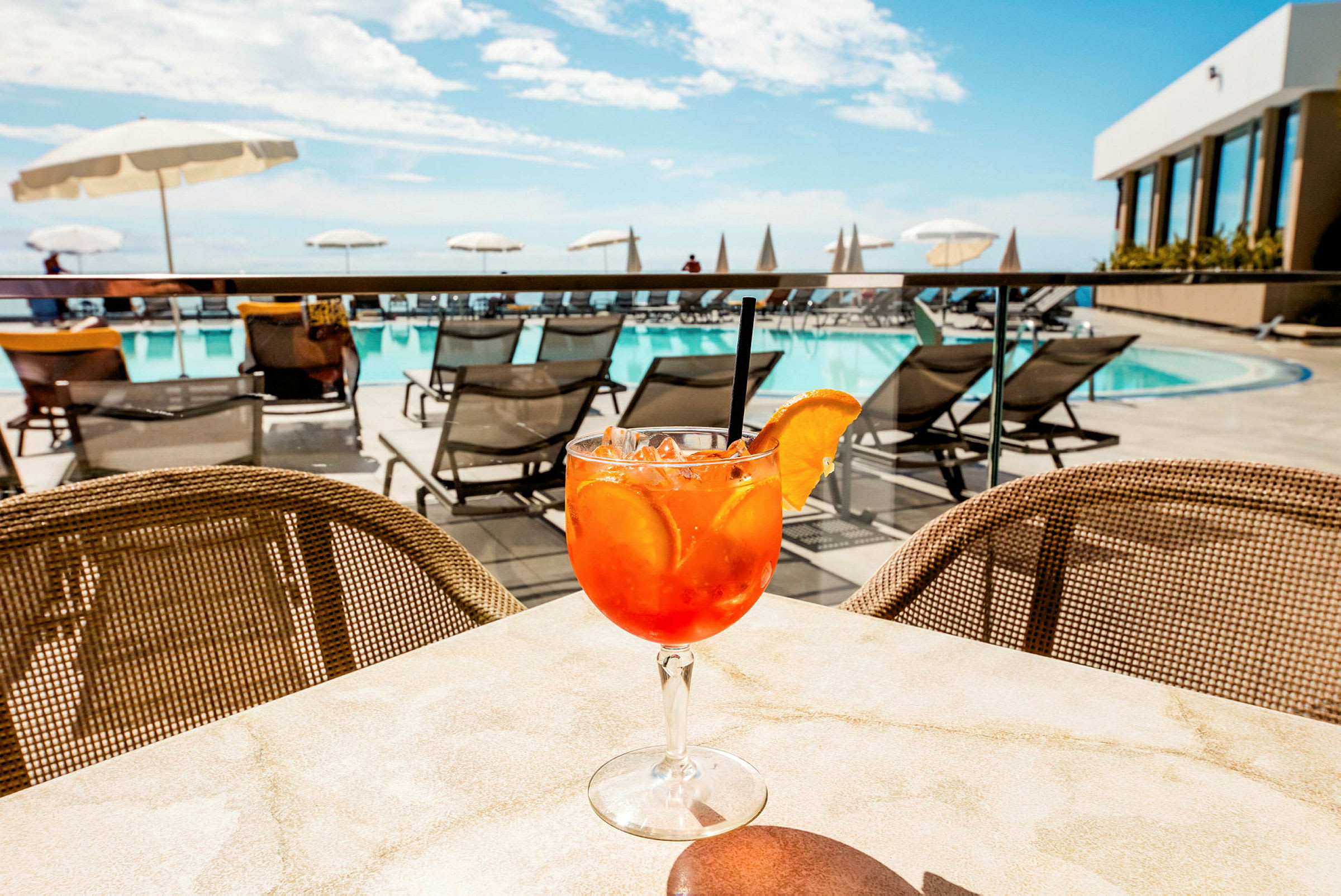 Ett glas med en orange dryck dekorerad med en apelsinskiva på ett bord nära en pool. (AI-genererad text)