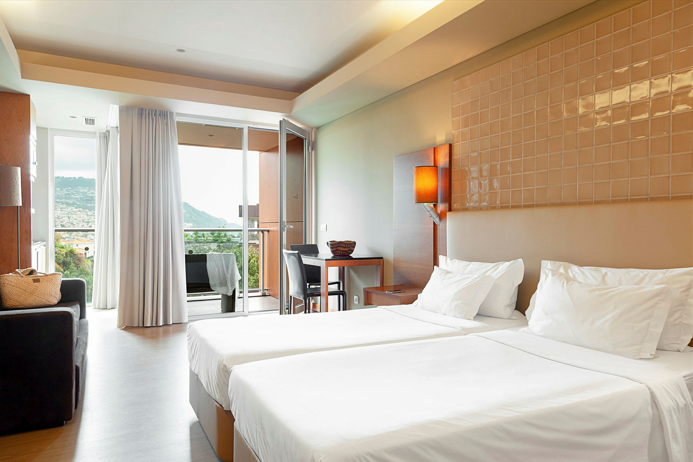 Hotellrum med två enkelsängar, sittgrupp och utsikt mot en bergig miljö genom glasdörr. (AI-genererad text)
