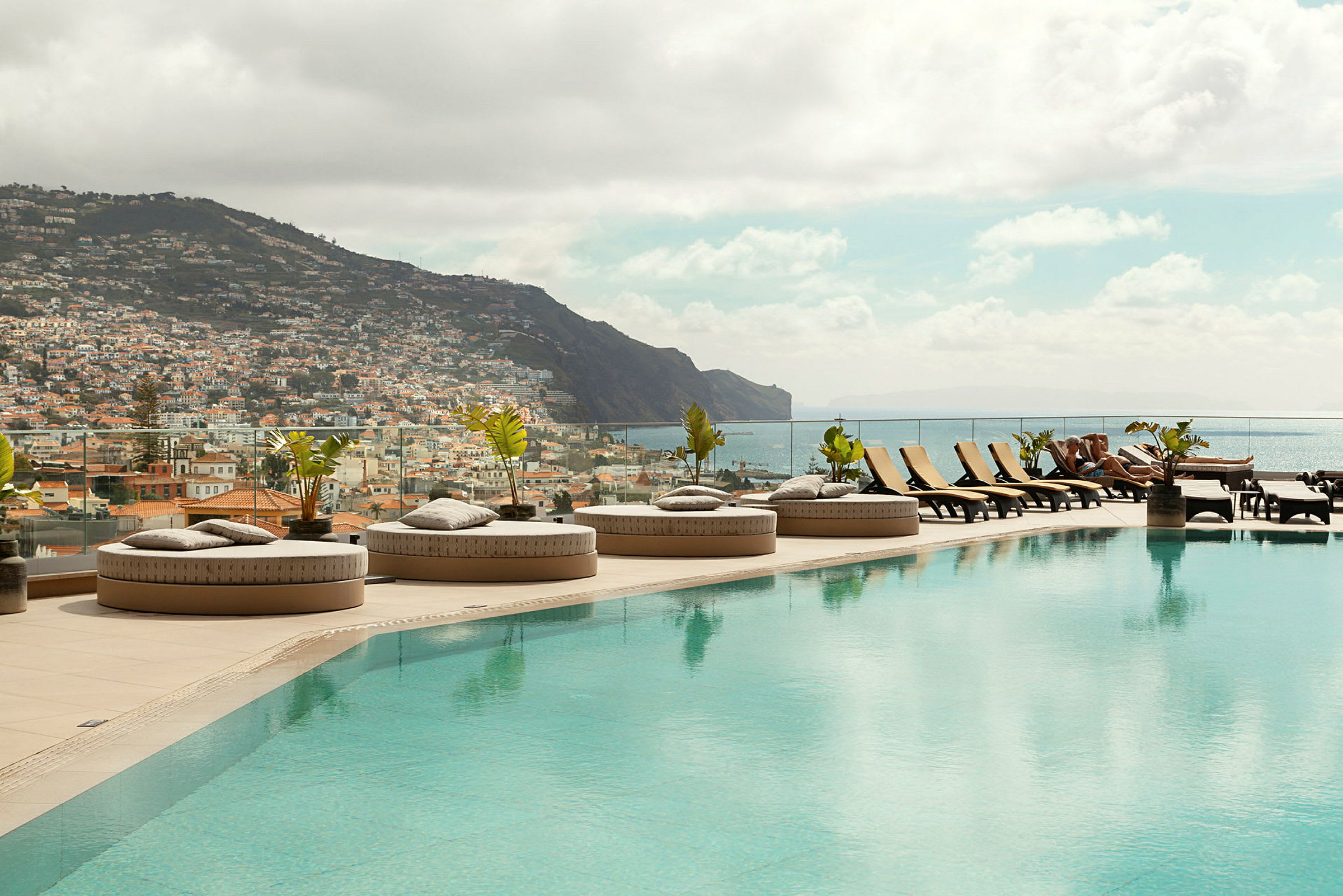 En infinitypool med solstolar och utsikt över en stad och berg. (AI-genererad text)