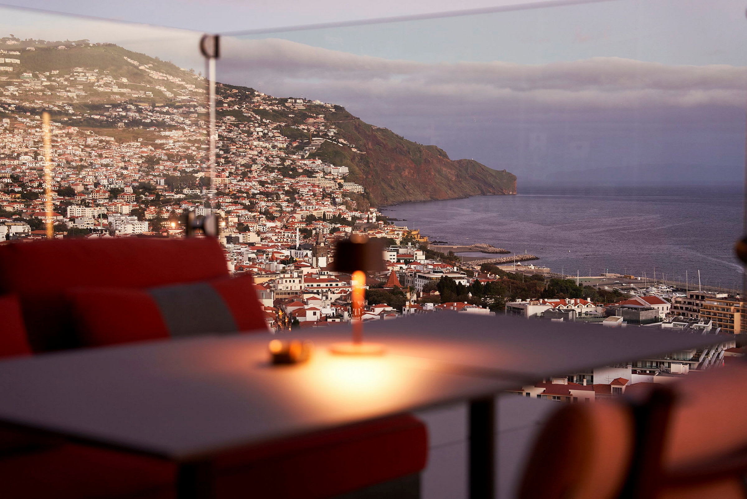 Utsikt över en kuststad med en bergssluttning och havet i bakgrunden, sett från en restaurang med röda sittplatser. (AI-genererad text)