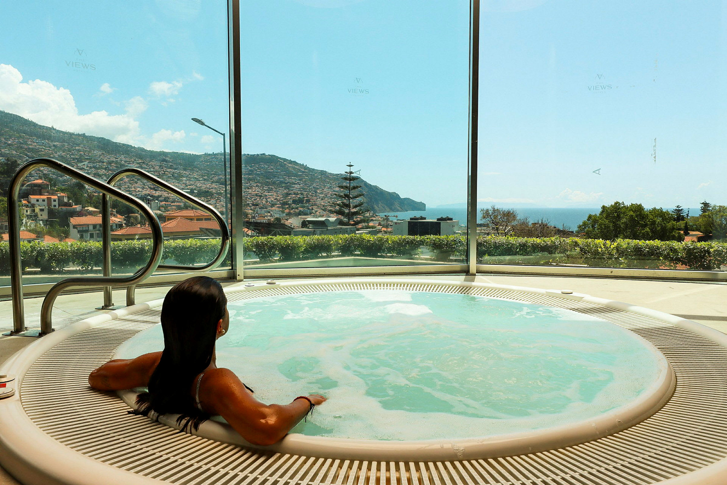 En person sitter i en bubbelpool med utsikt över havet och en stad. (AI-genererad text)