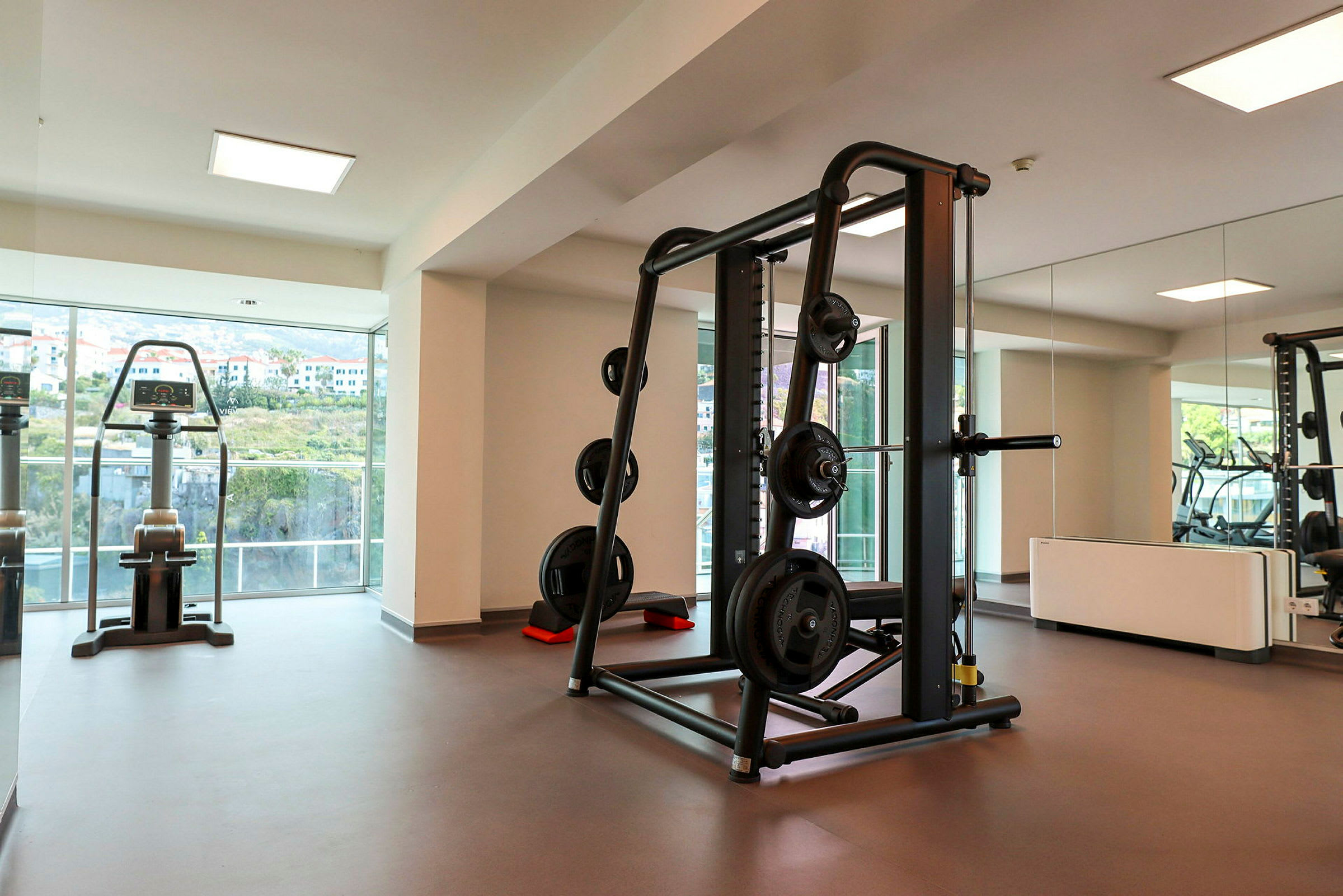 Ett gym med styrketräningsutrustning och fönster med utsikt. (AI-genererad text)