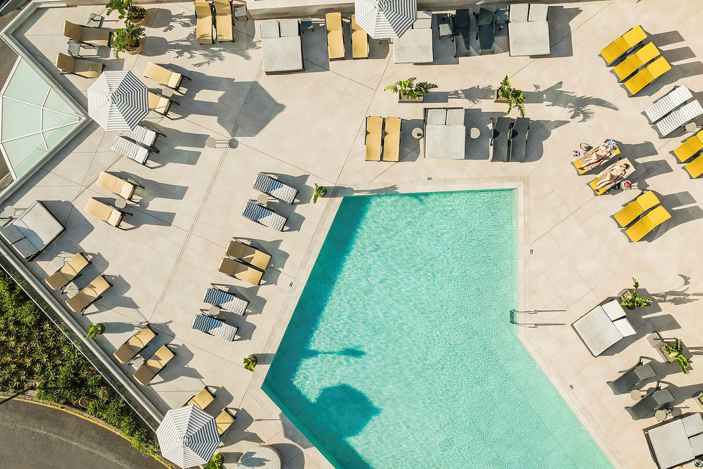 Vy ovanifrån av en pool med omgivande solstolar och parasoller. (AI-genererad text)